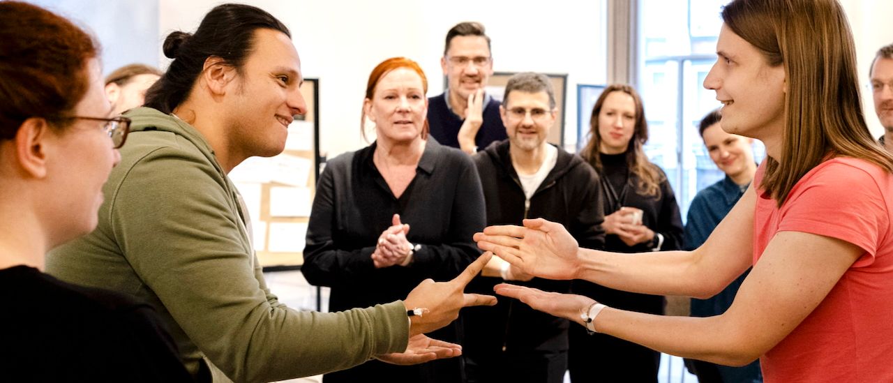 Teamentscheidungen und Zusammenarbeit stärken – Softwareentwicklung im Unternehmen verankern Zwei Teammitglieder spielen Schere-Stein-Papier, umgeben von applaudierenden Kolleg:innen – Symbol für gemeinsames Entscheiden und Teamstärkung