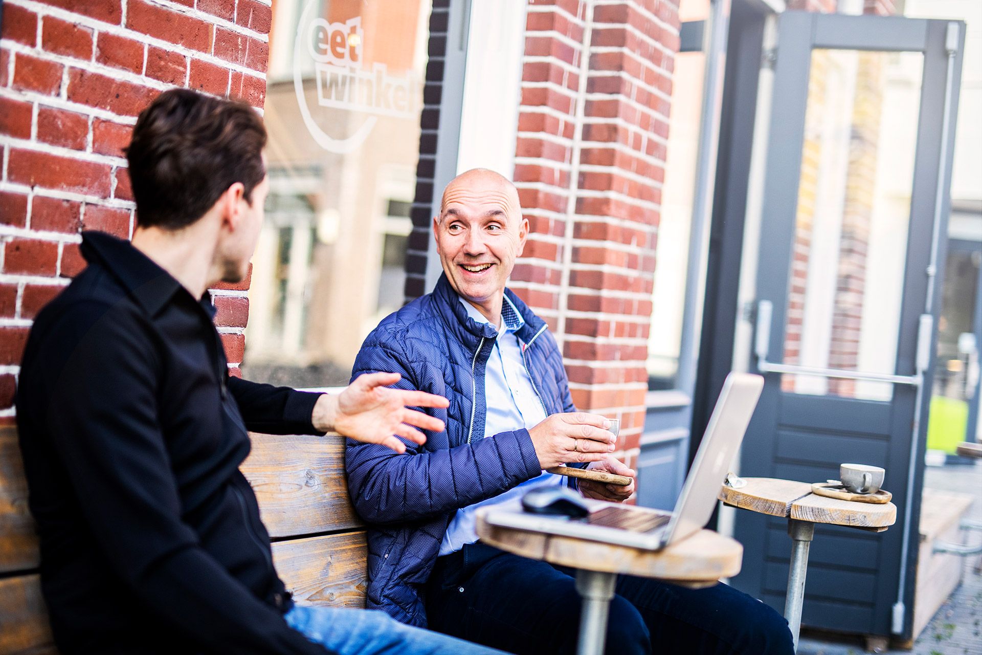 Twee mannen praten aan een tafel buiten op een terras