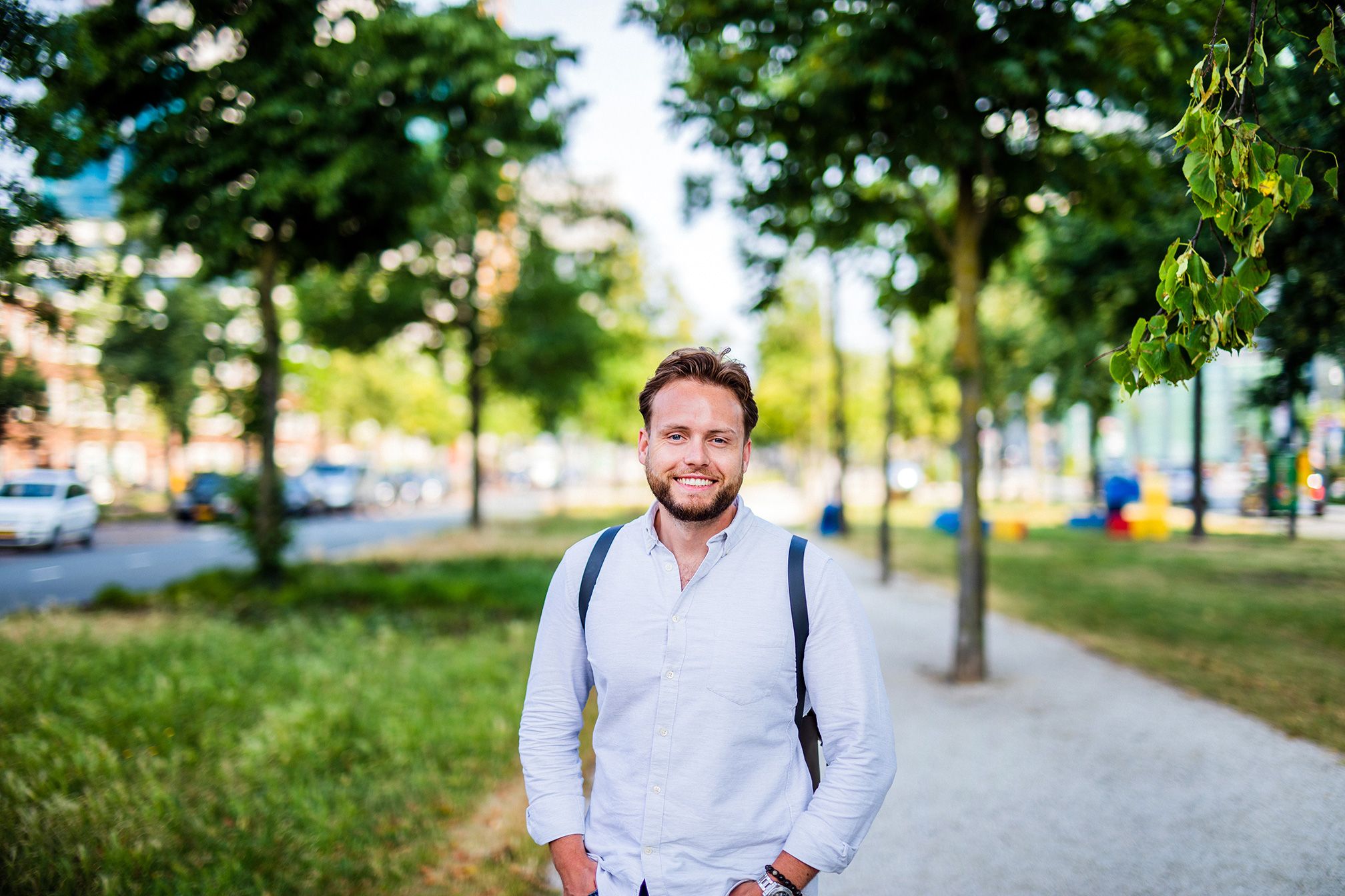 Young men is standig outside in a park and smiles into the camera