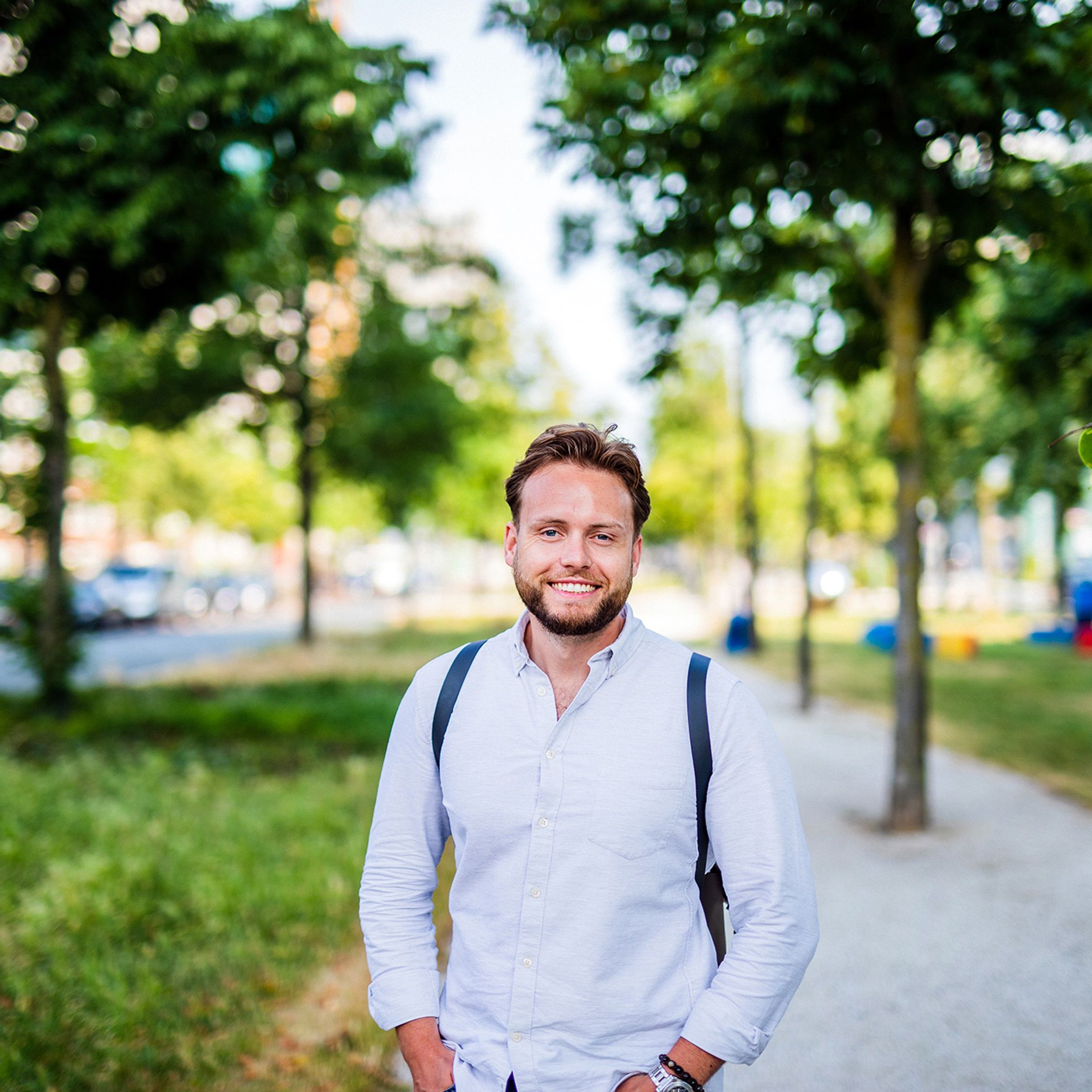 Young man is standing outside and smiles in the camera
