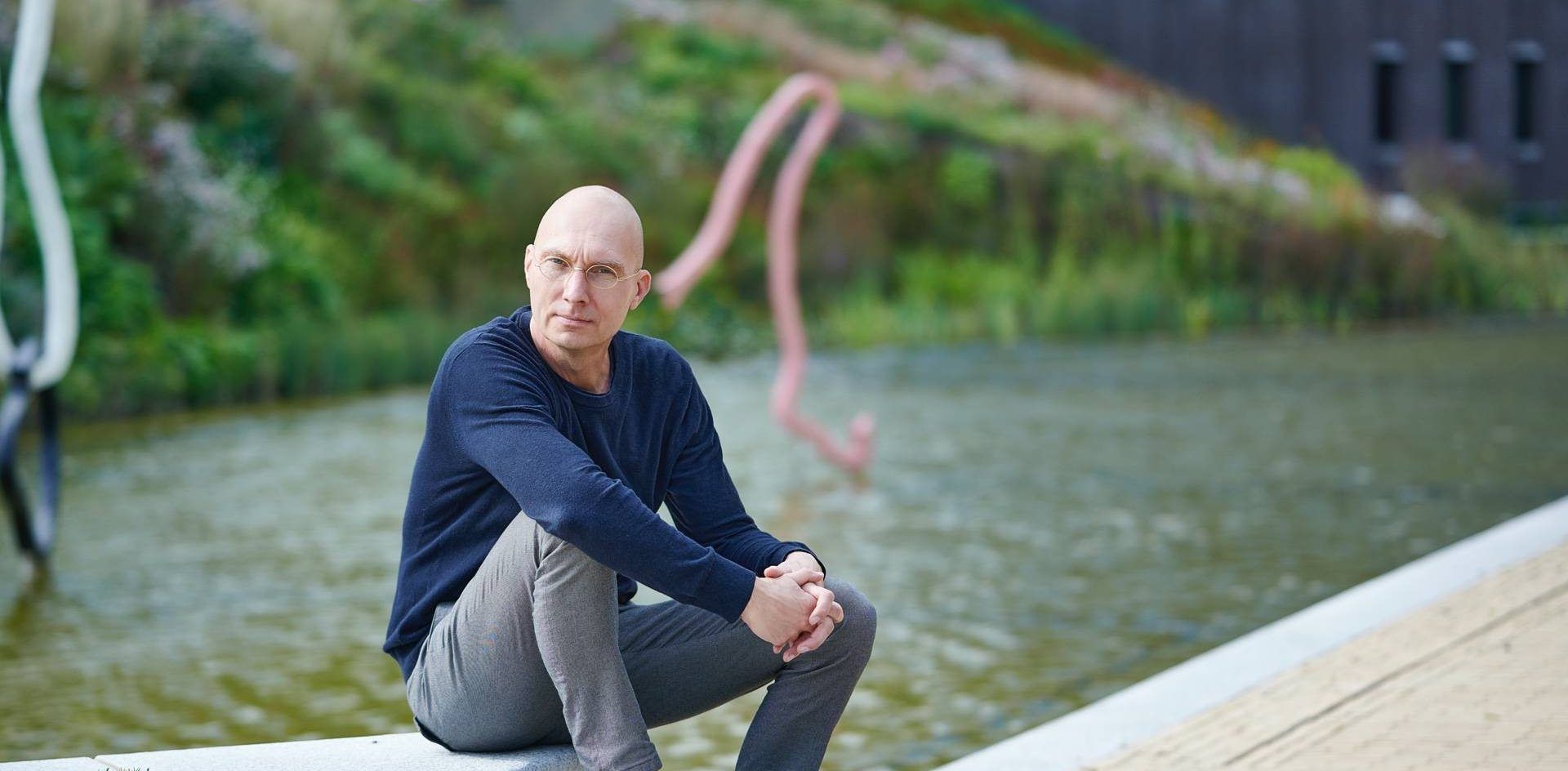 Man poseert voor vijver in Rabobank tuin