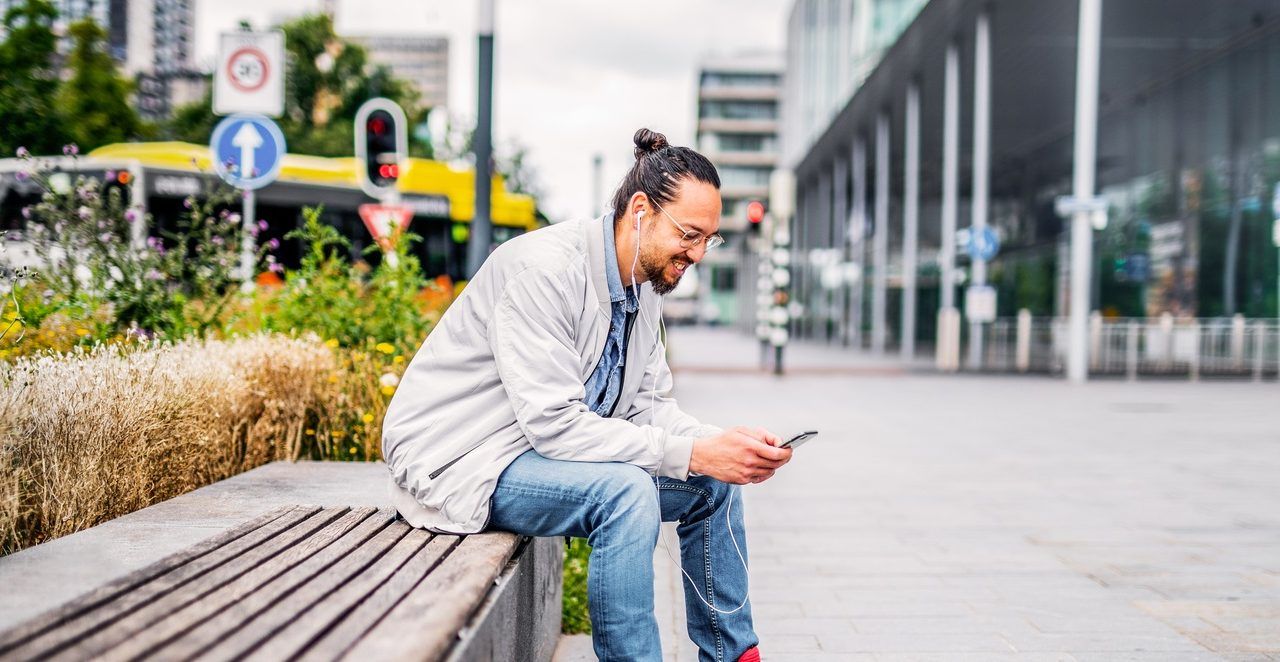 Man sits on bench and looks at cell phone.