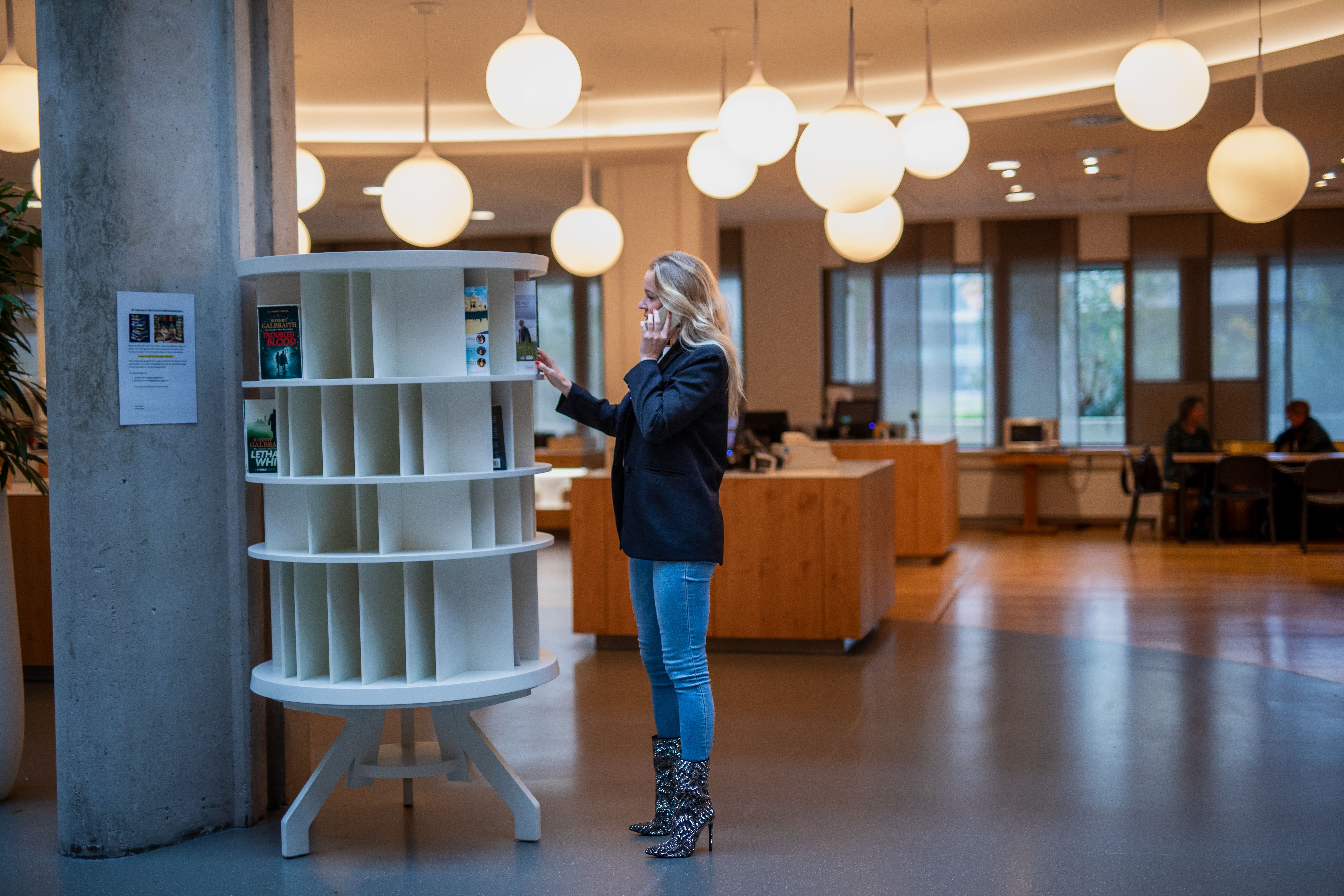 Vrouw belt terwijl ze door boekenkast bladert