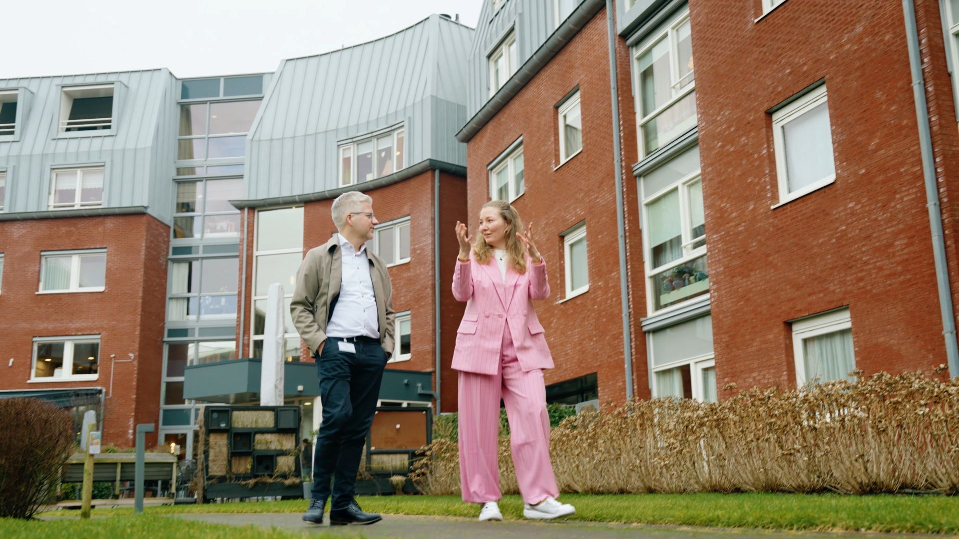 Kelly en de interviewer staan in een nieuwbouwbuurt en praten met elkaar