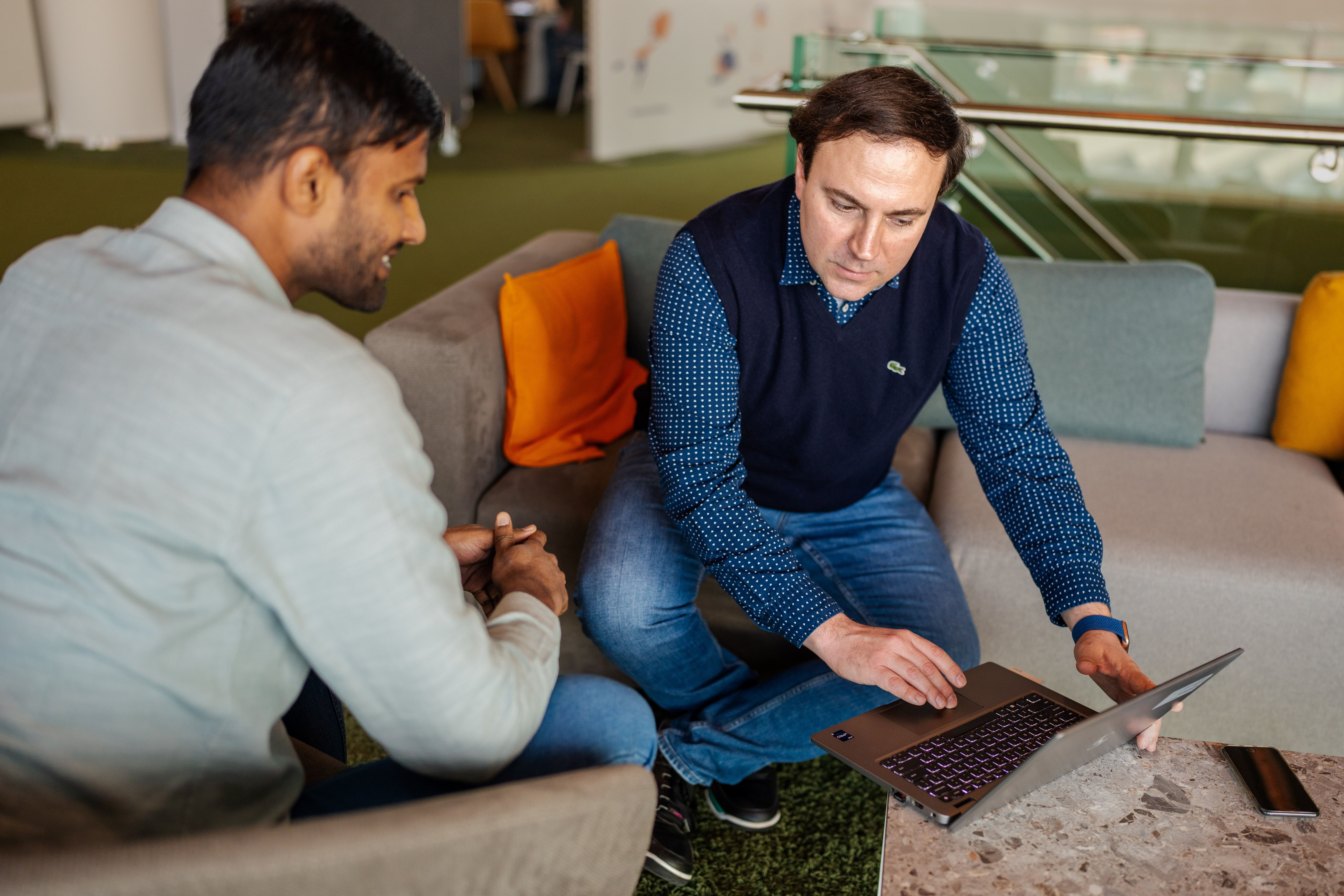 two men sitting on a couch and looking at a laptop