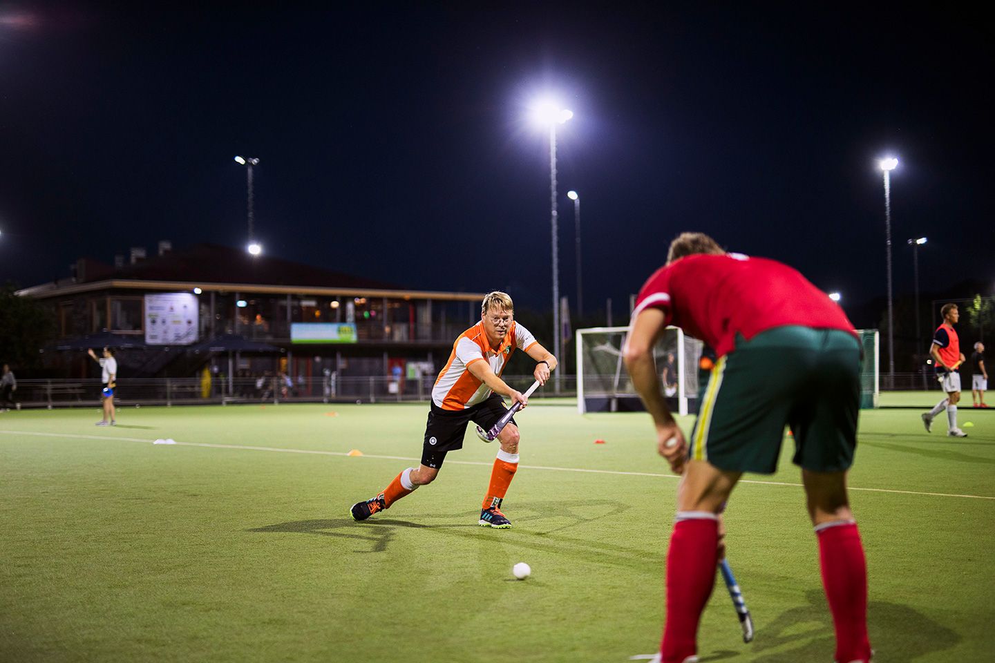 Man in oranje-wit shirt speelt hockey.