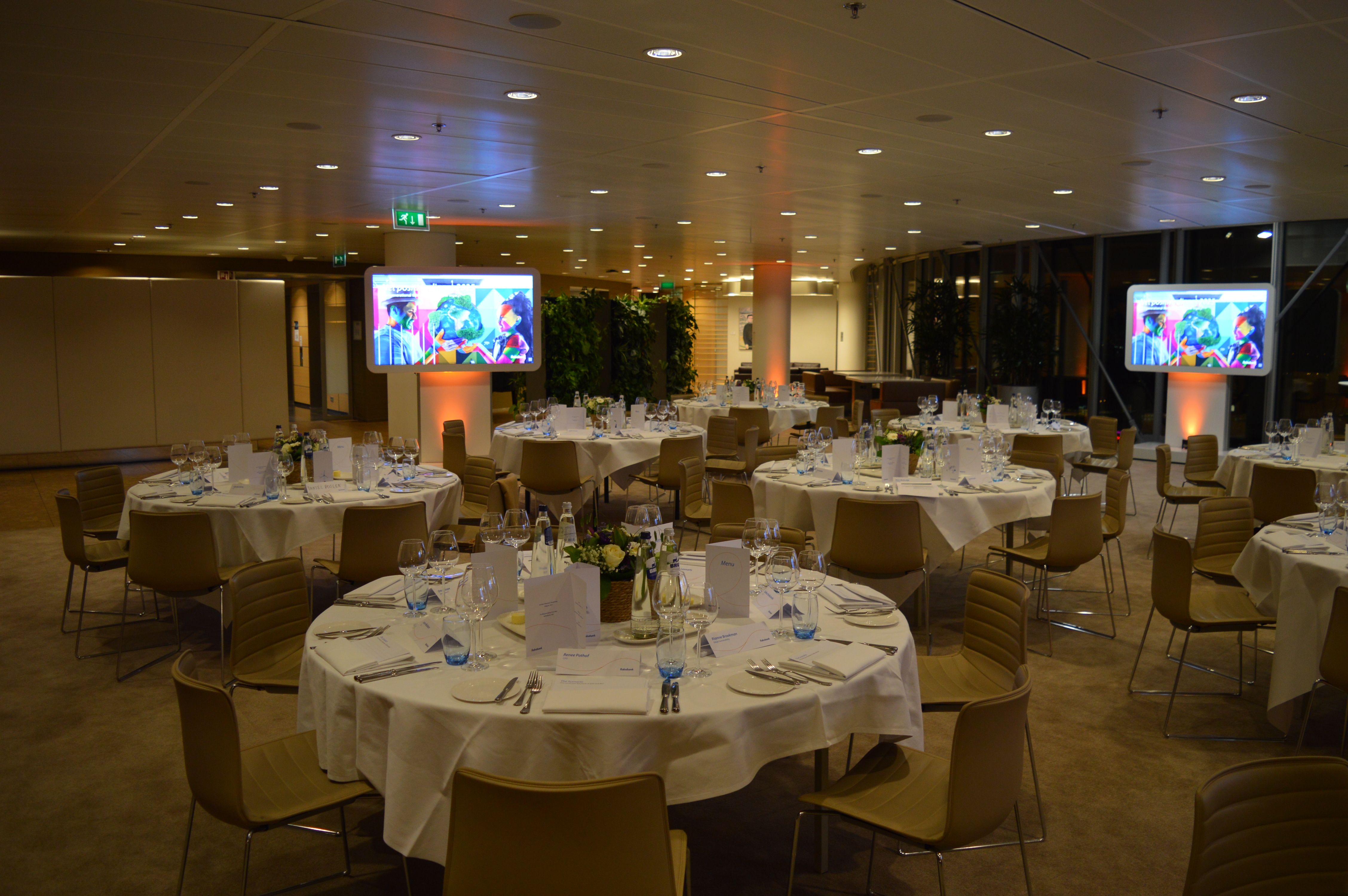 Een zaal met mooie gedekte tafels met presentatie schermen aan de zijkant