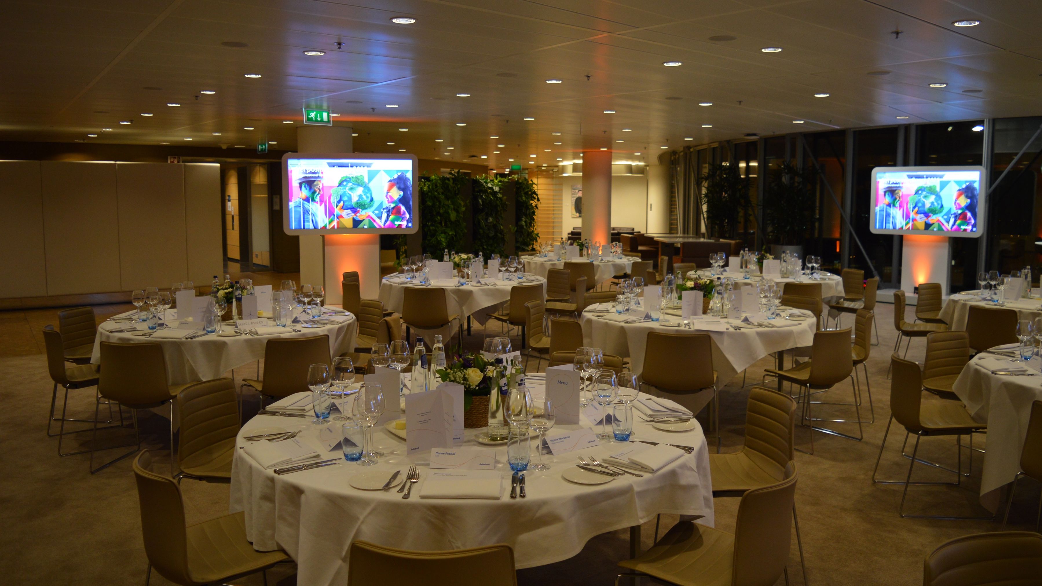 Een zaal met mooie gedekte tafels met presentatie schermen aan de zijkant