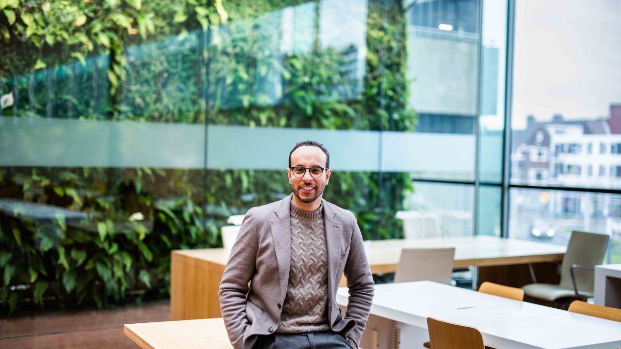 Jonge man zit op bureau voor groene achtergrond met planten