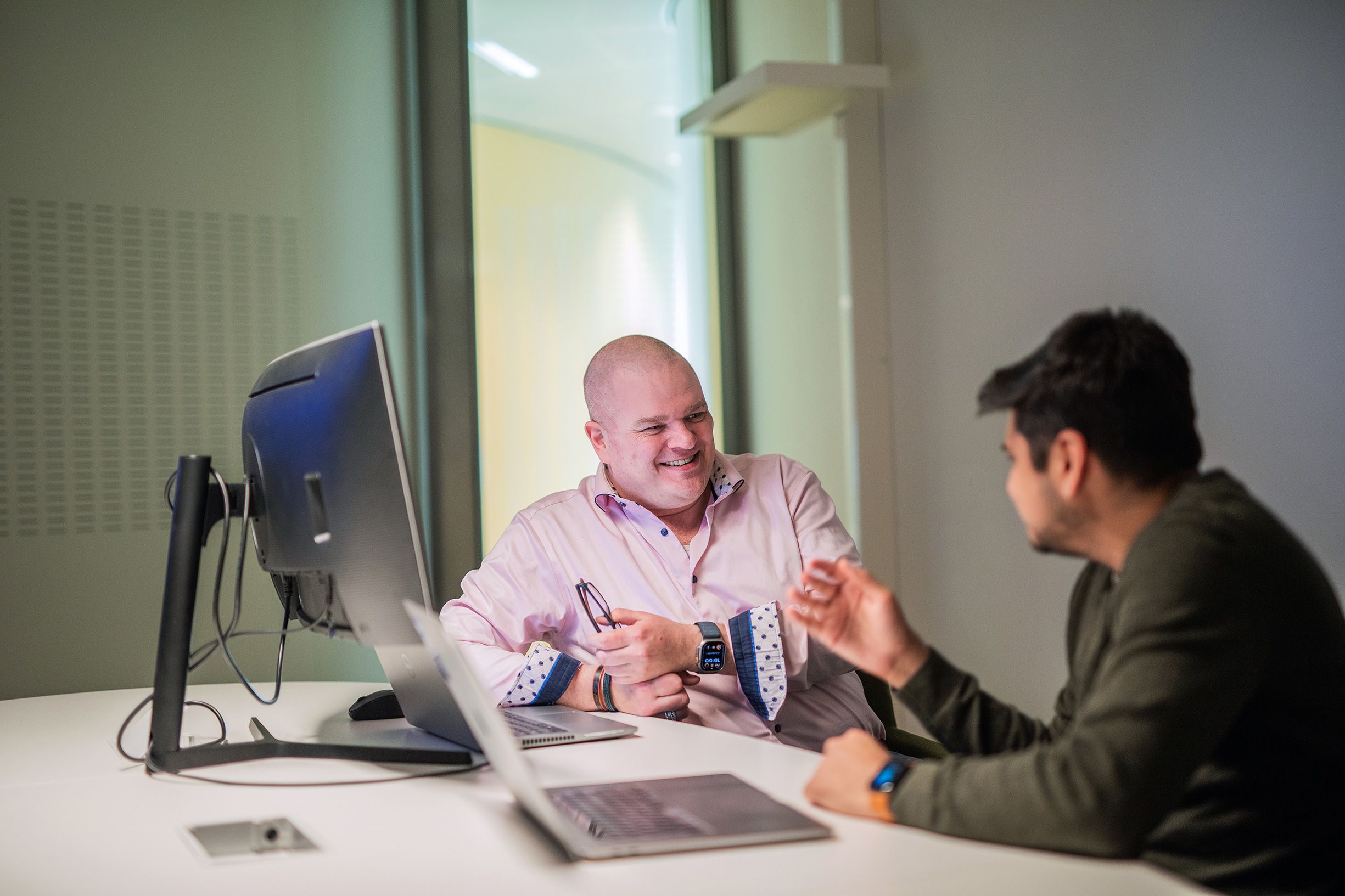 Two people in conversation at white office desk with computers.