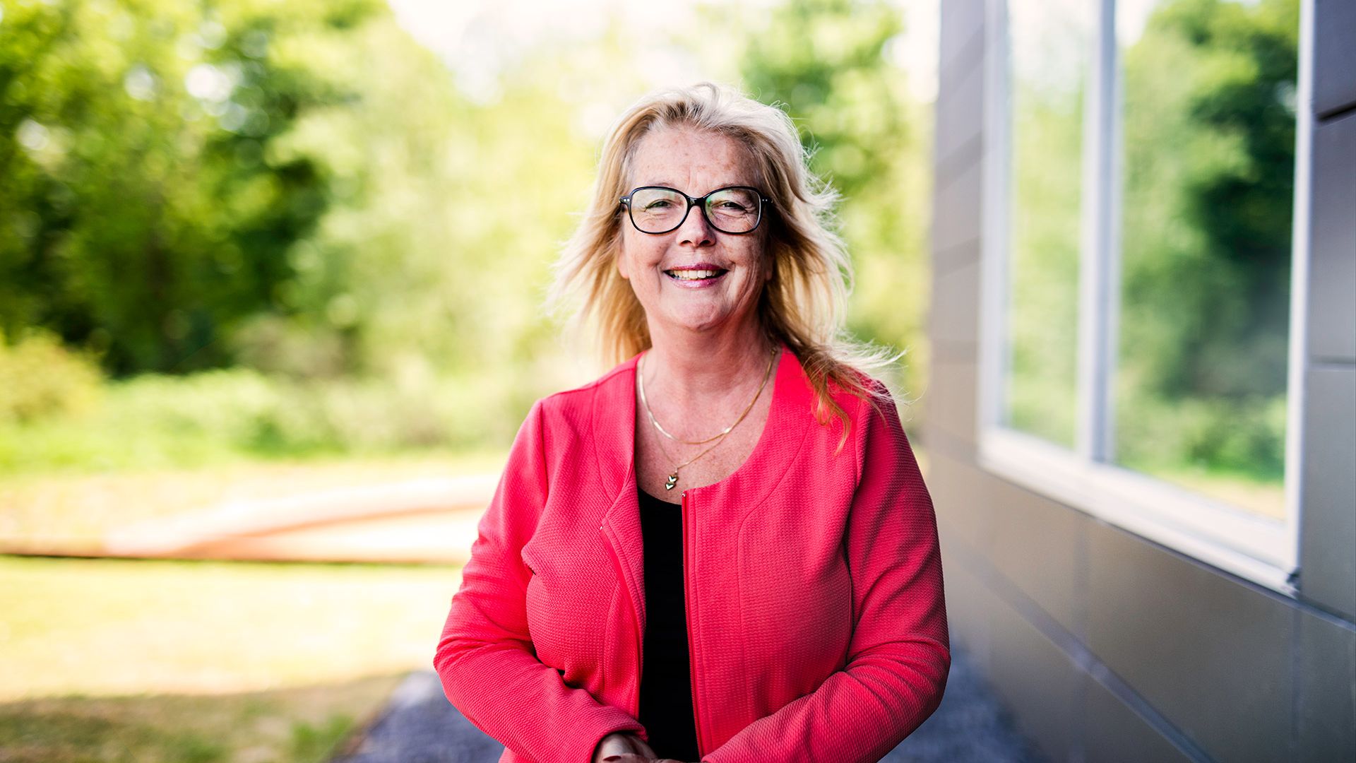 Carolien buiten naast gebouw in groene omgeving