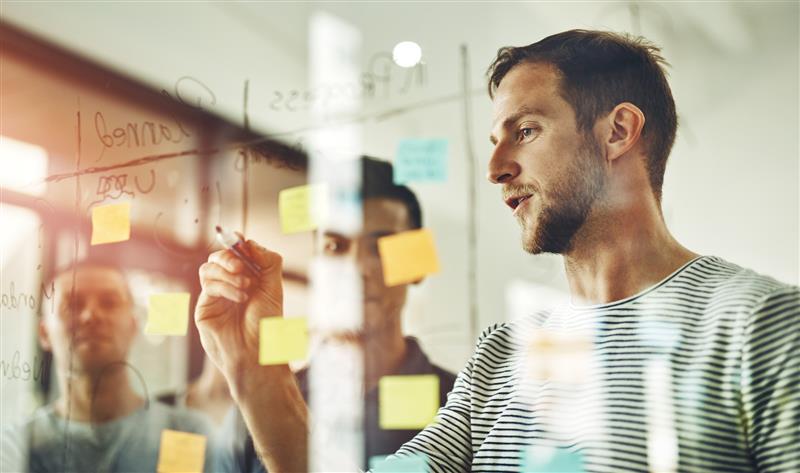 Mannen brainstormen met post it's op een raam