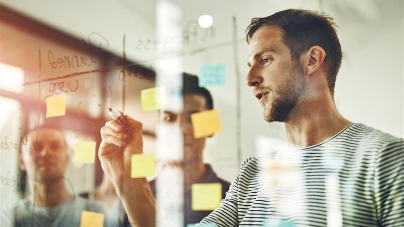Mannen brainstormen met post it's op een raam