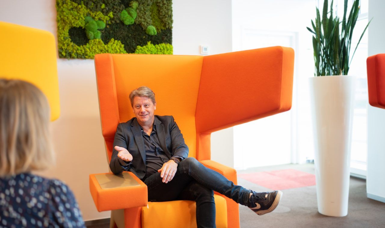 Man sits in an orange chair talking to a woman