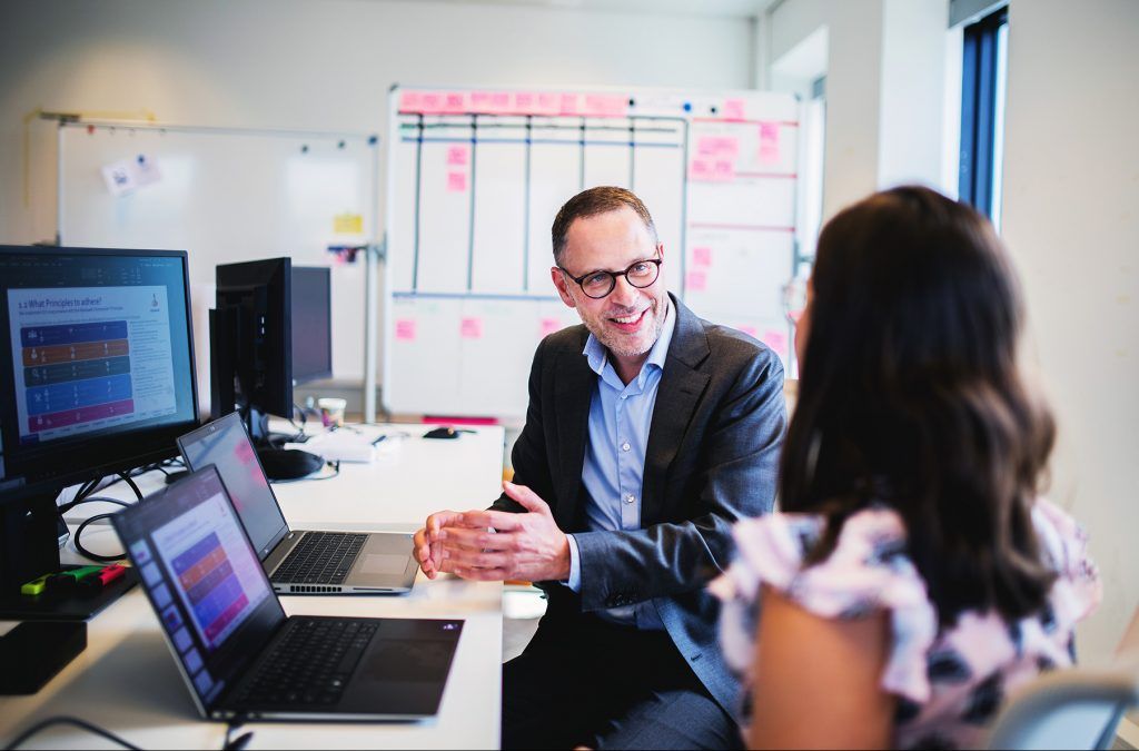 Man in overleg met vrouwelijke collega achter bureau