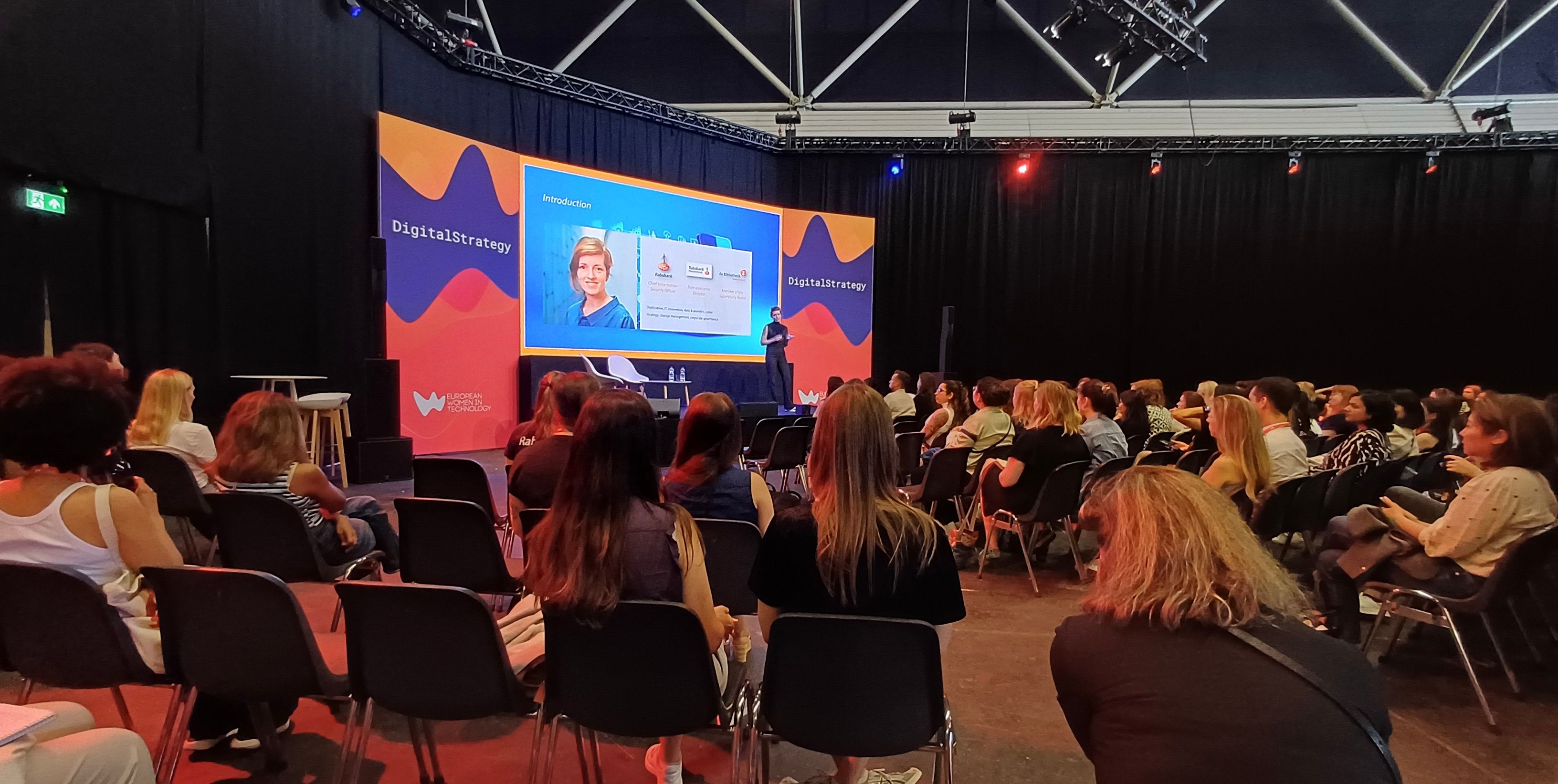 Corence Klop is standing on stage giving a presentation in front of an audience.