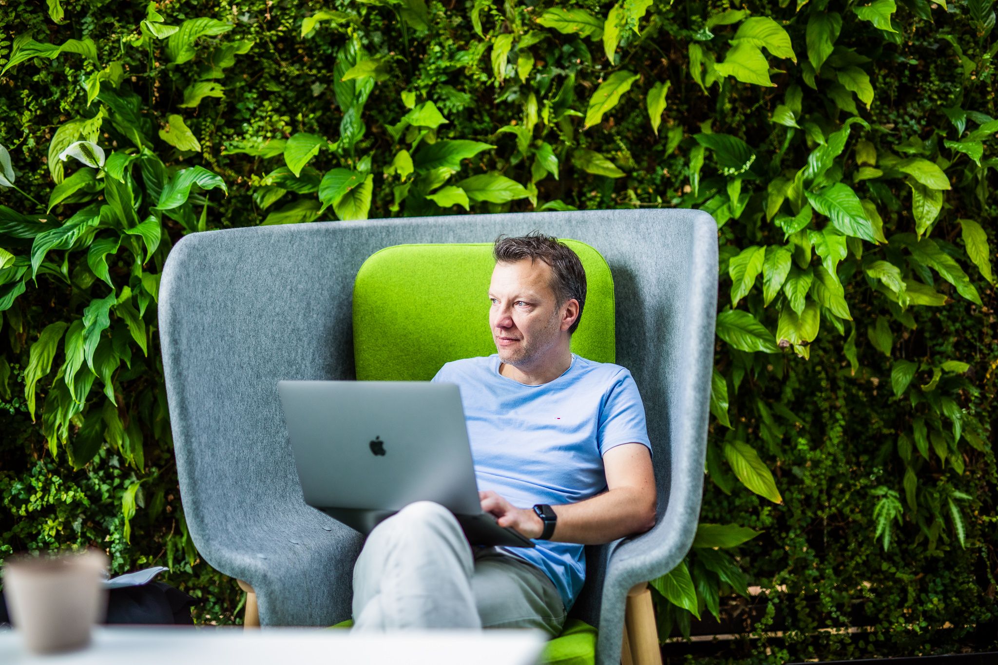 Chris sits on a chair with a laptop in a room with plants