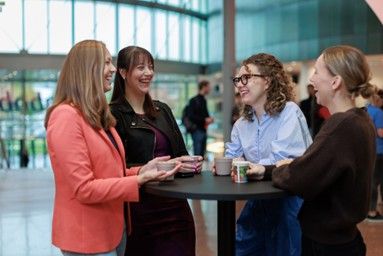 Four women drinking coffee and having conversation together, laughing, in a Rabobank office building  