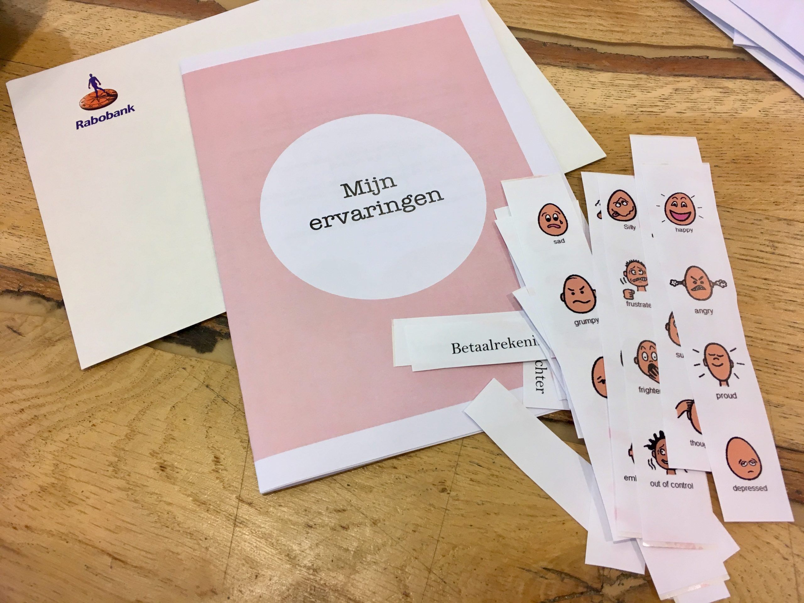 An envelope, a printed paper booklet and cut out pictures expressing emotions.