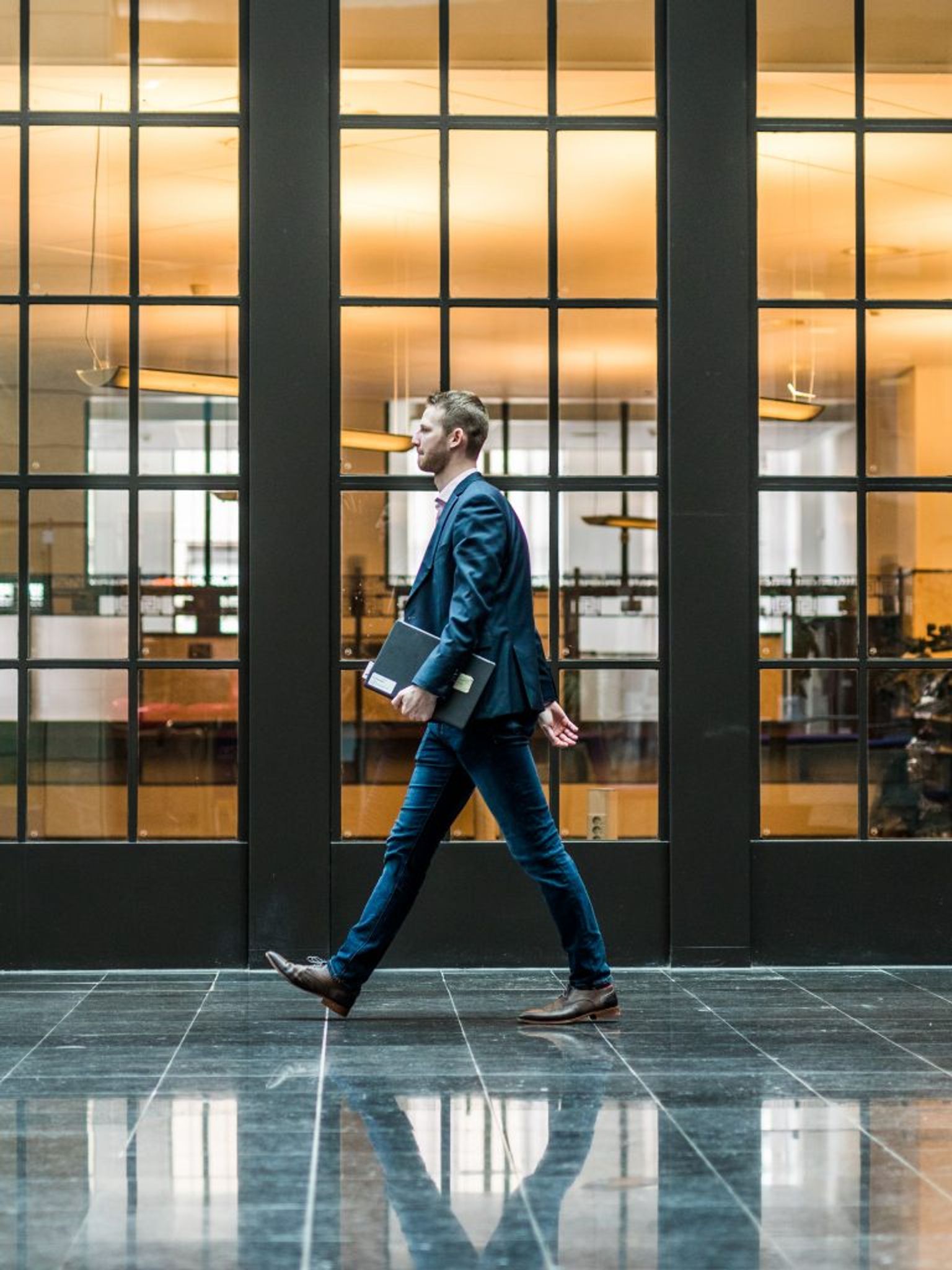 Man loopt door gang langs hoge glazen ramen.