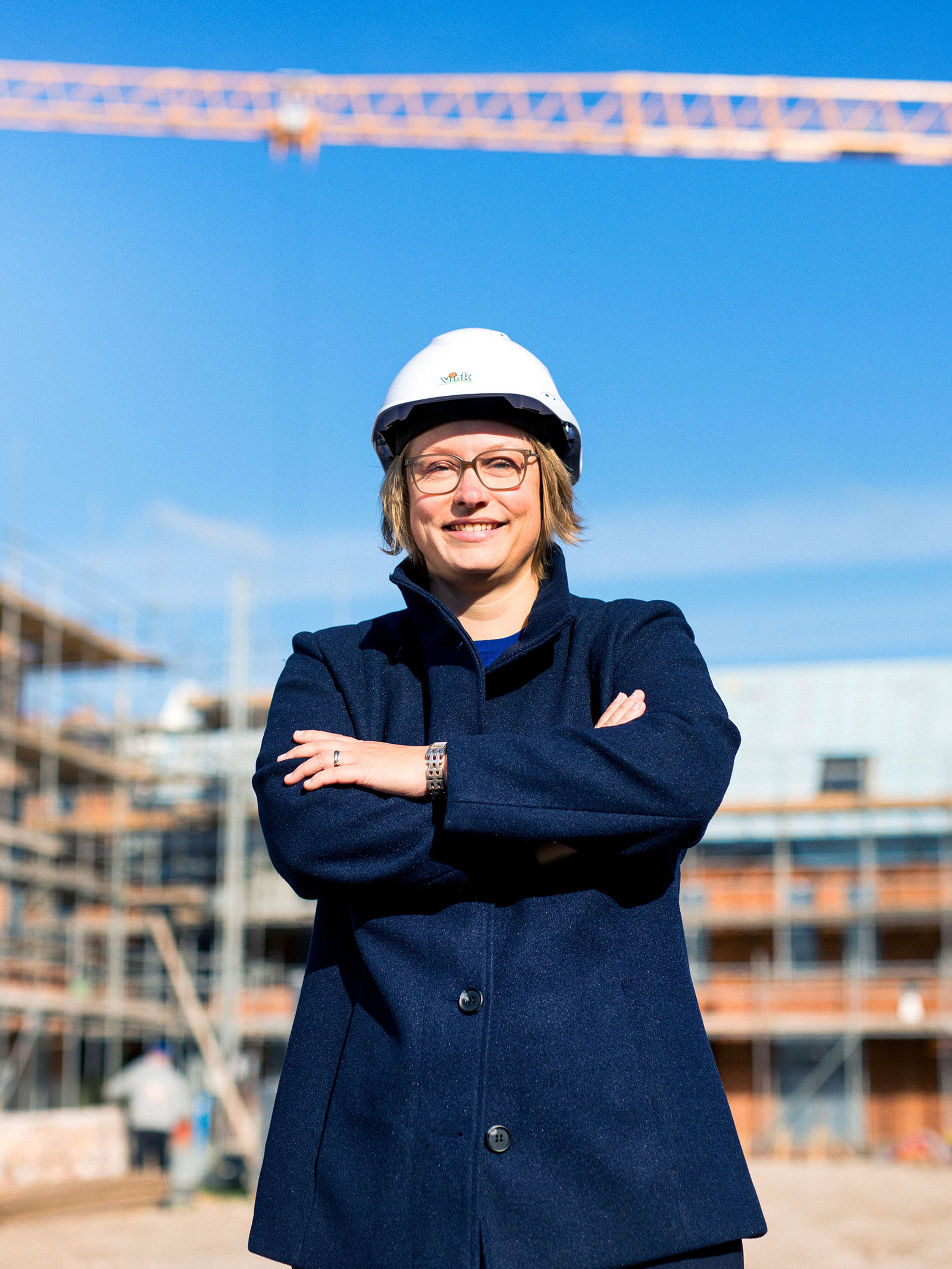 Ellen Posthoorn with construction helmet in front of new construction homes and crane.