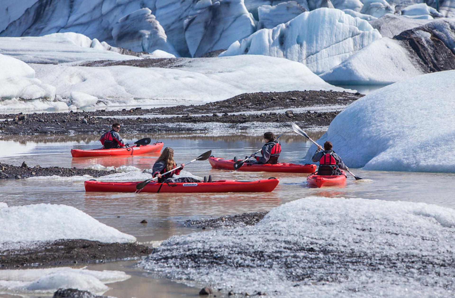 People on red kayaks paddling through some icebergs.