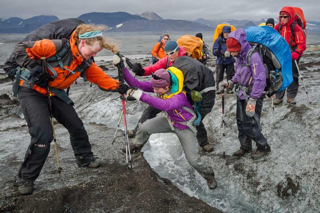 Hikers helping each other navigate over rocks, emphasizing teamwork during a hike in Iceland.