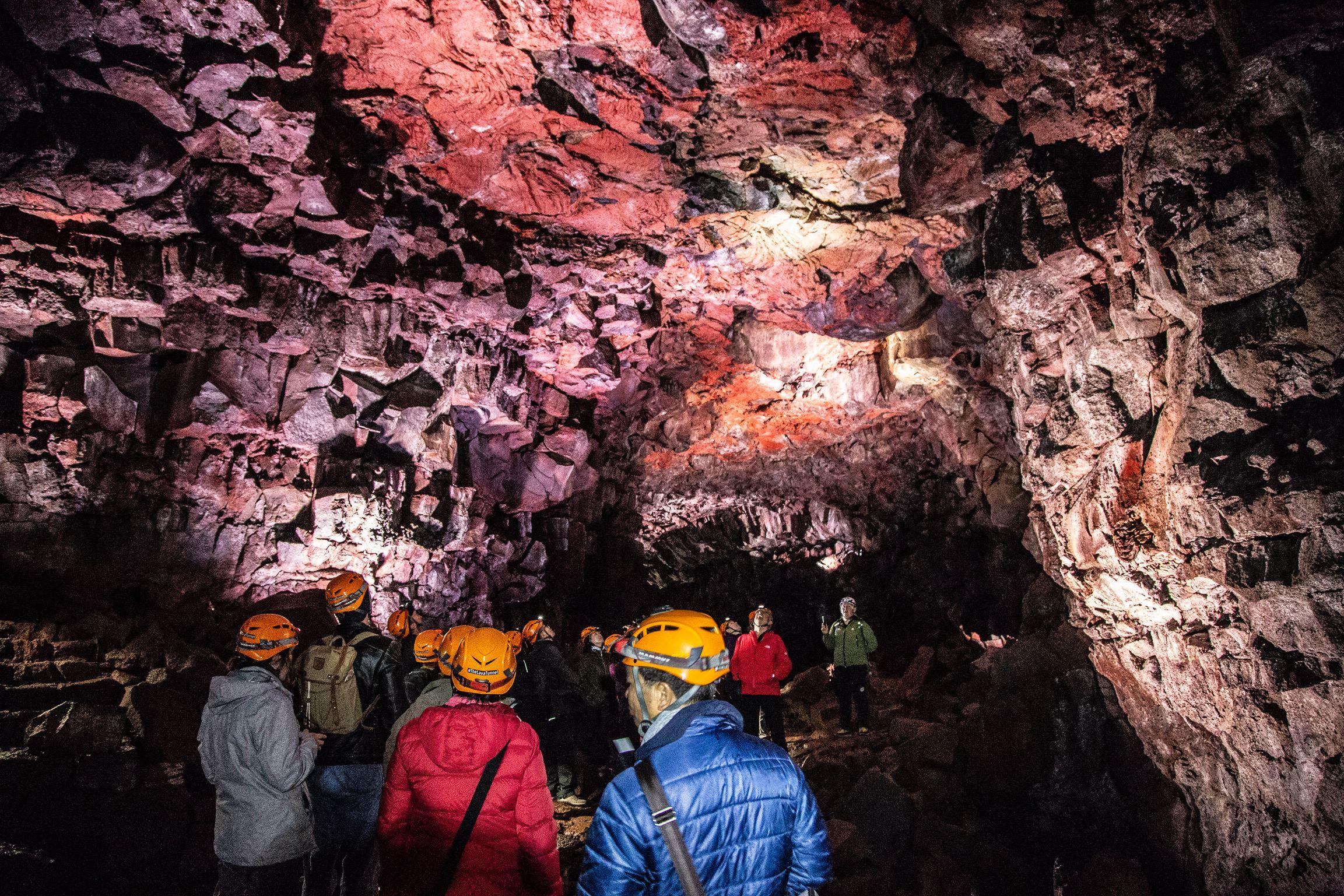 A group of people inside the lava tunnel listening to a caving guide in red jacket.