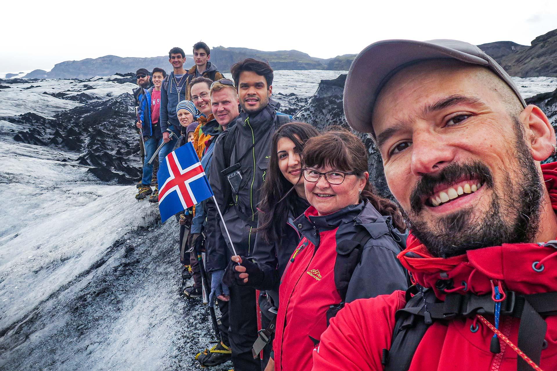 A guide with a group of people in a glacier in Iceland celebrating summer with the Icelandic flag