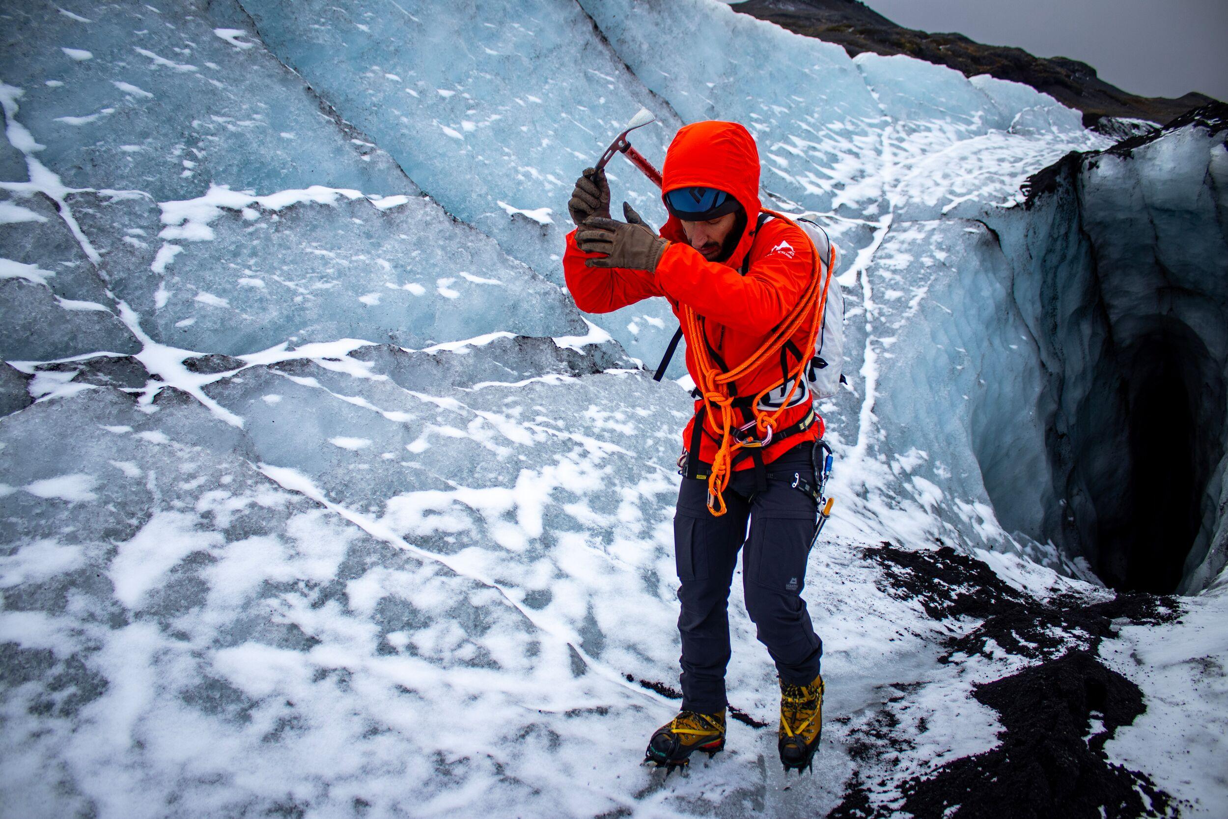 A glacier guide in a red jacket pulling out his ice axe while standing on a glacier