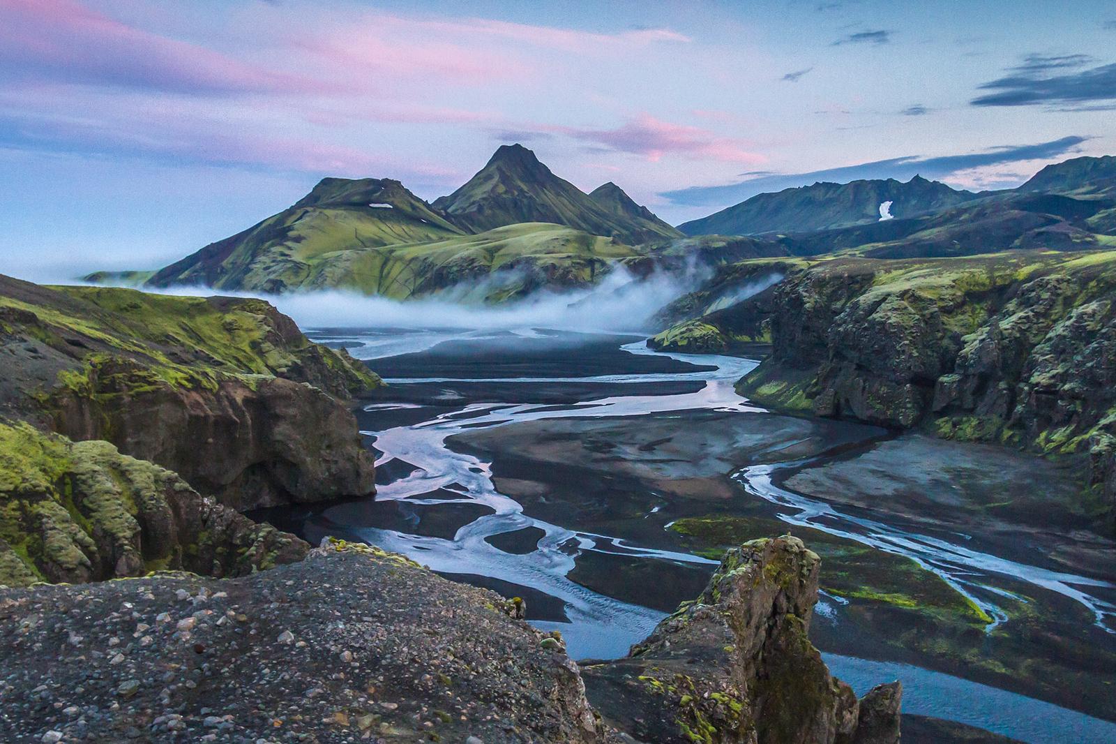 A beautiful mountain valley with rivers flowing everywhere and the light blue sky above with pink clouds
