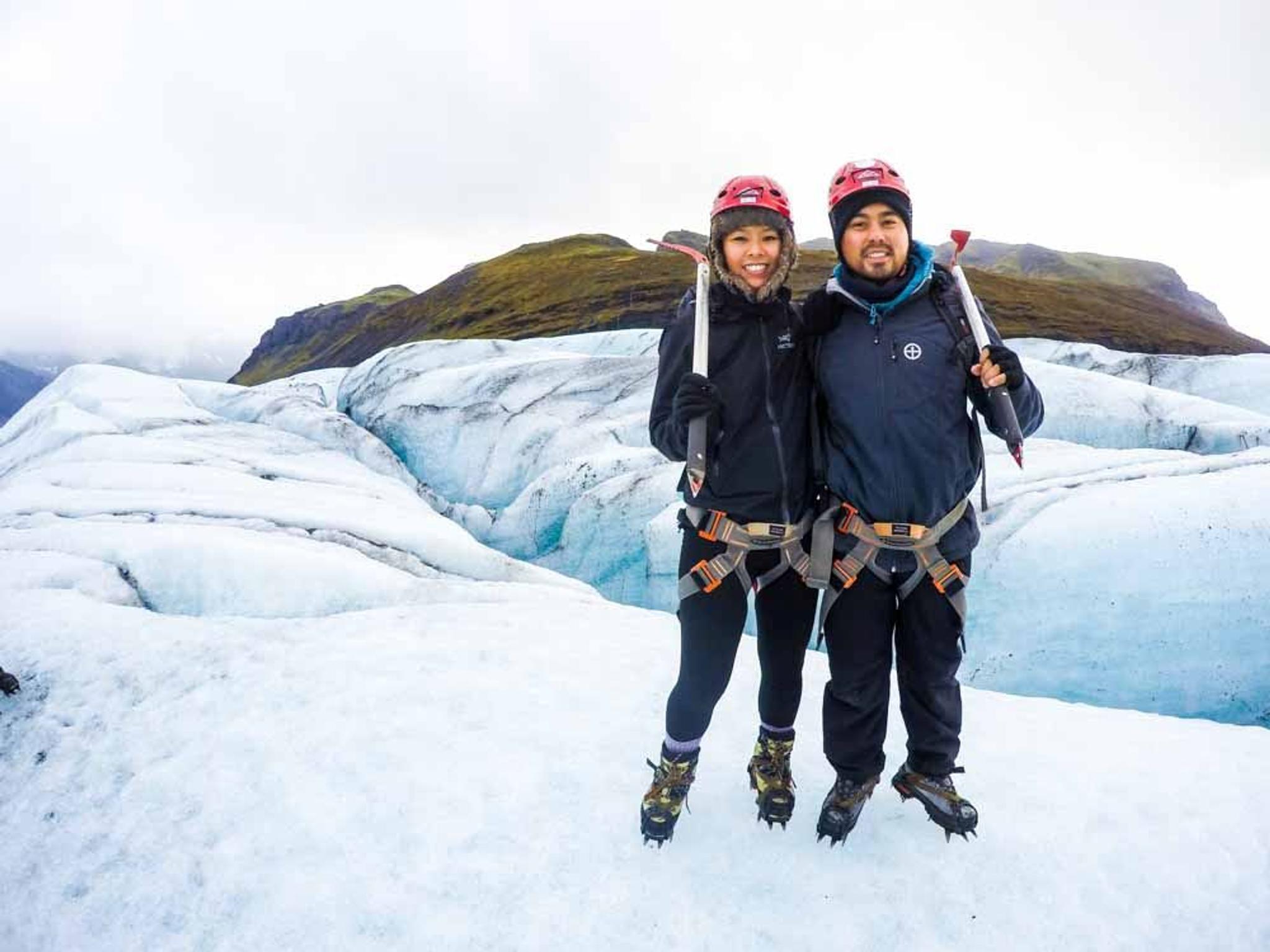 A couple carrying ice axes and helmets during a glacier walk.