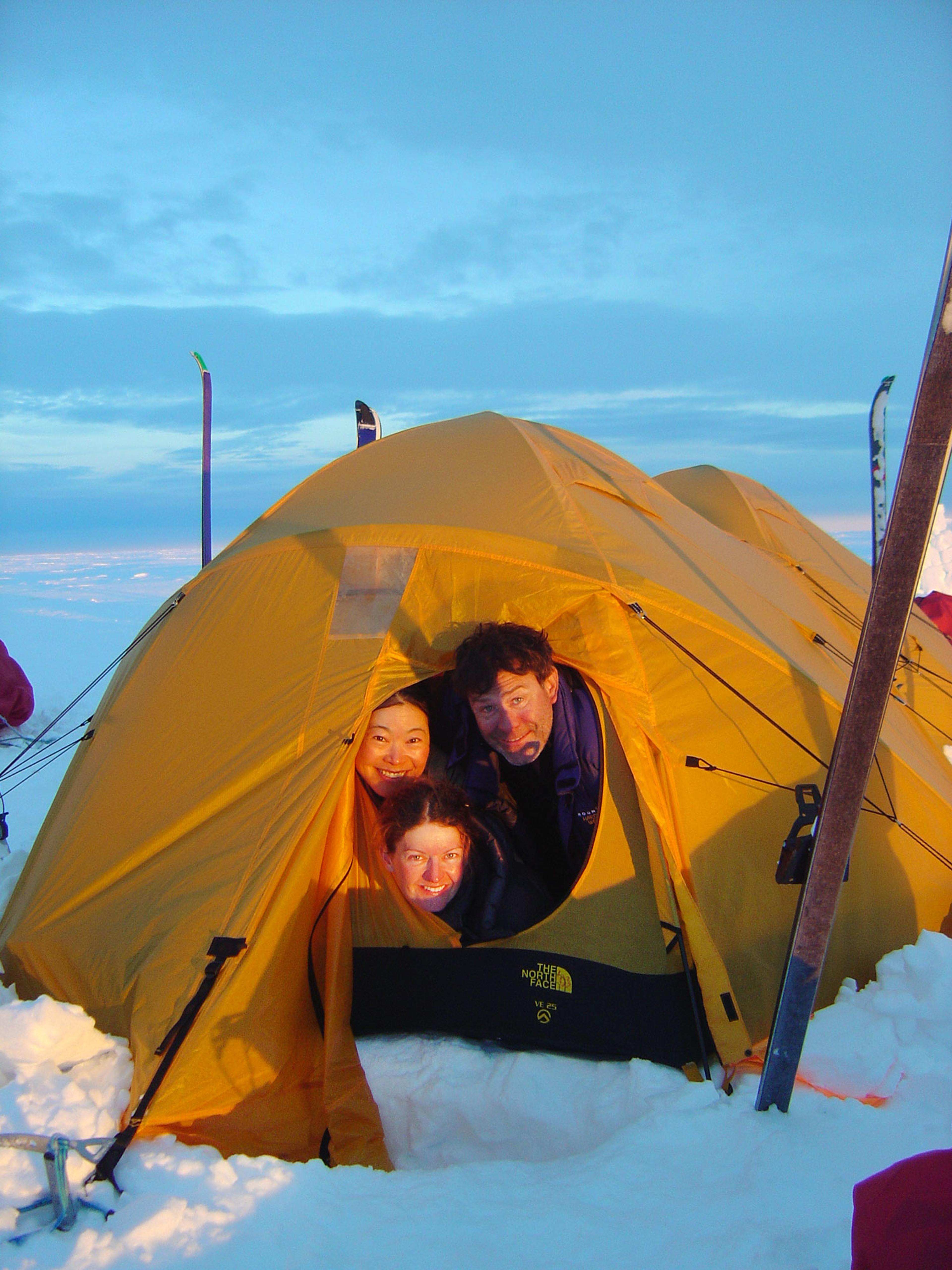 Three happy people peeking out of a tent on the glacier
