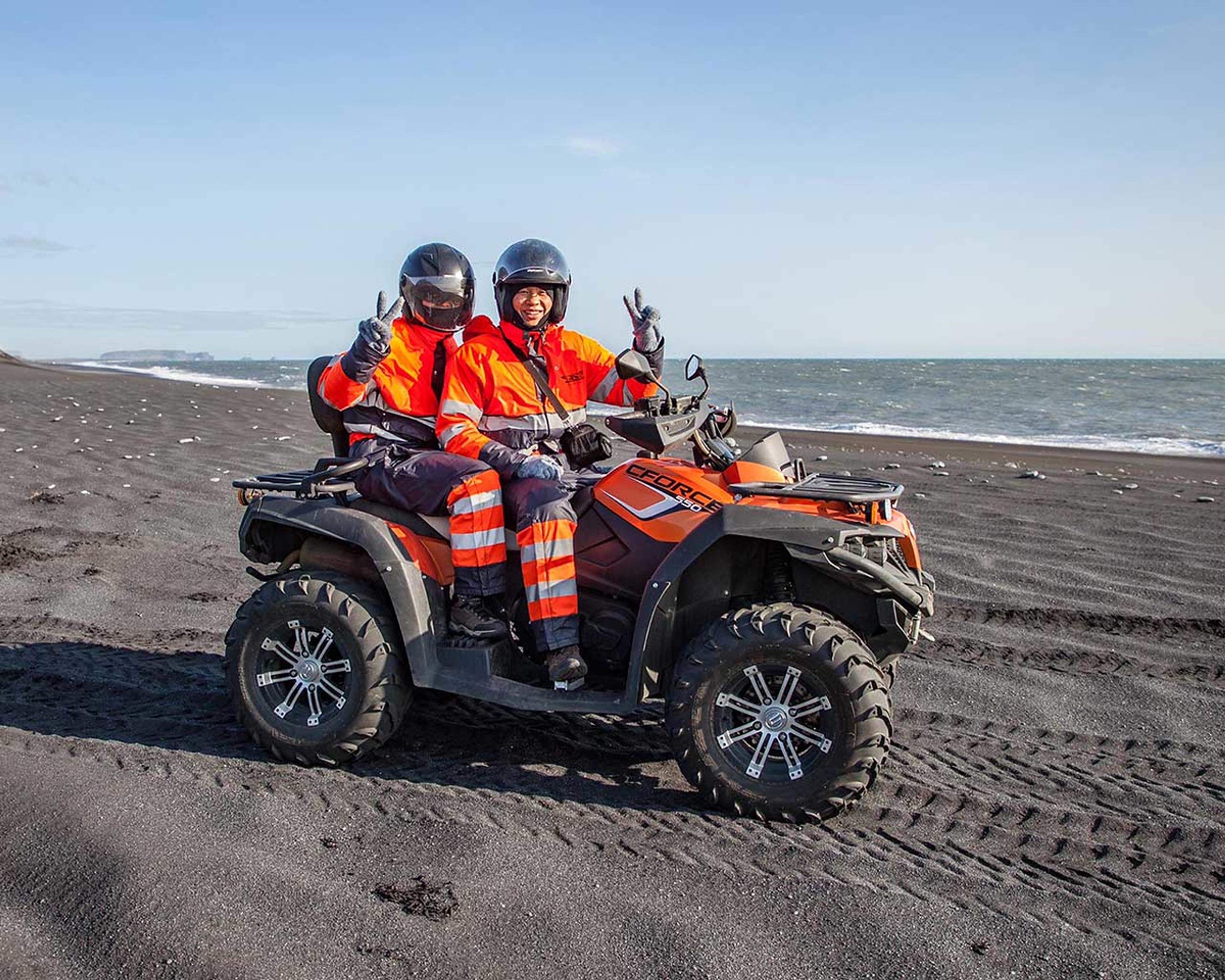 Two people smiling and happy sitting on a ATV quad bike on the black sand