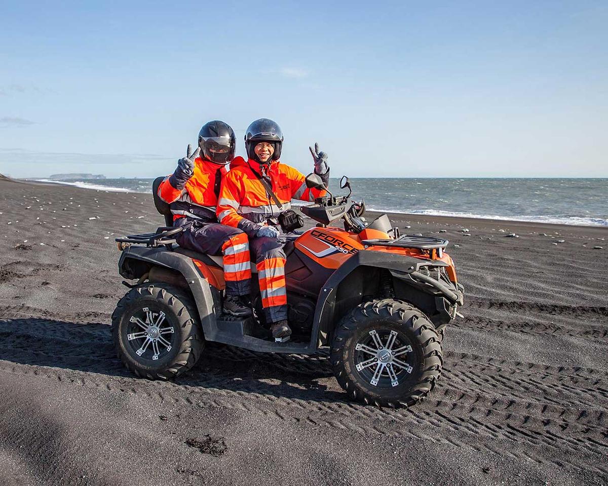 Two people smiling and happy sitting on a ATV quad bike on the black sand