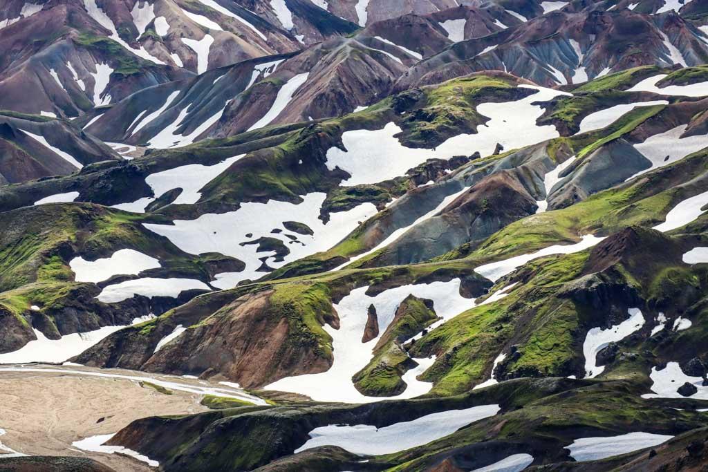 Aerial view of Landmannalaugar's colorful mountains with patches of green moss and snow creating a striking contrast.