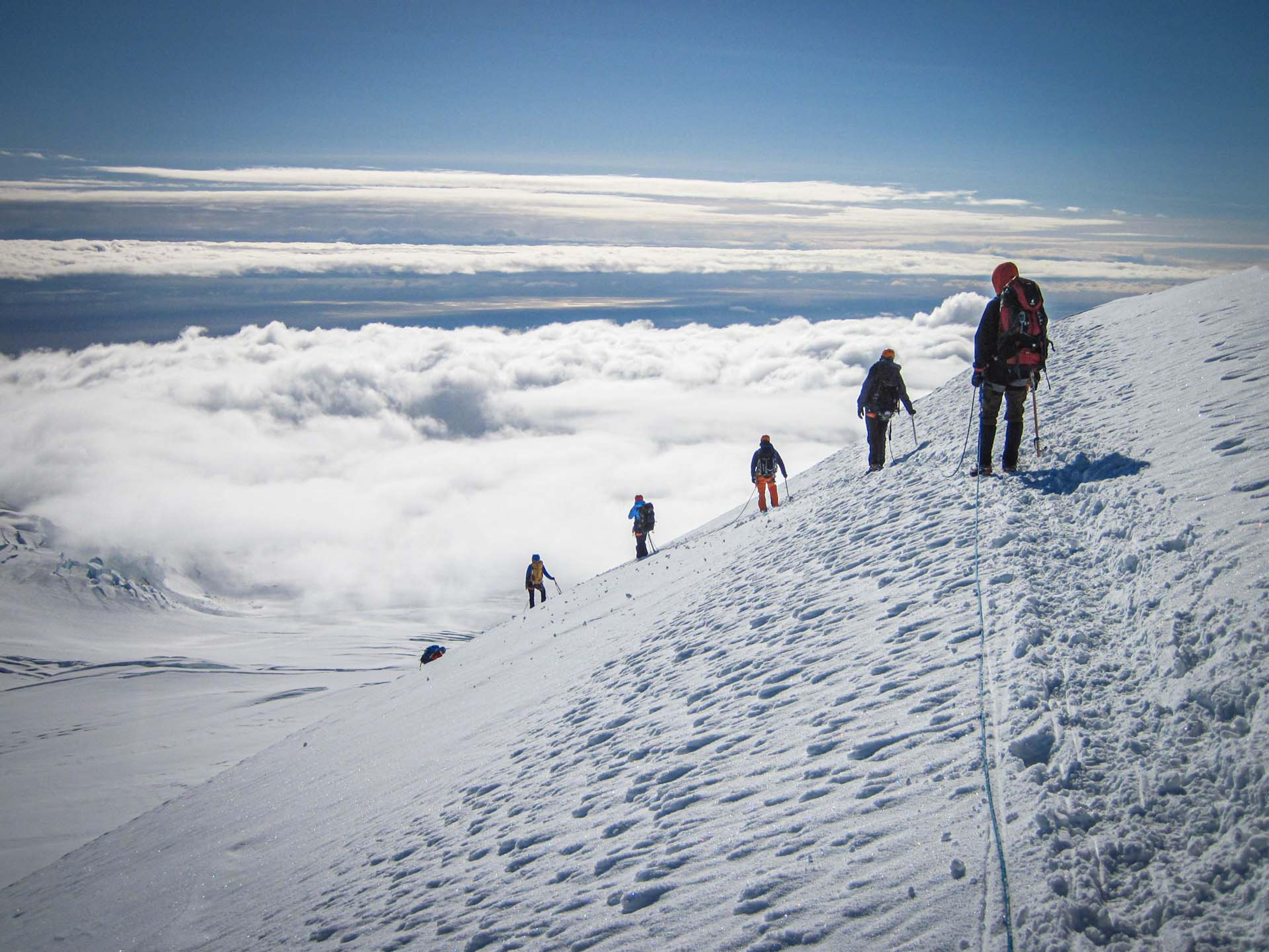 people doing down a snowy mountain above the clouds