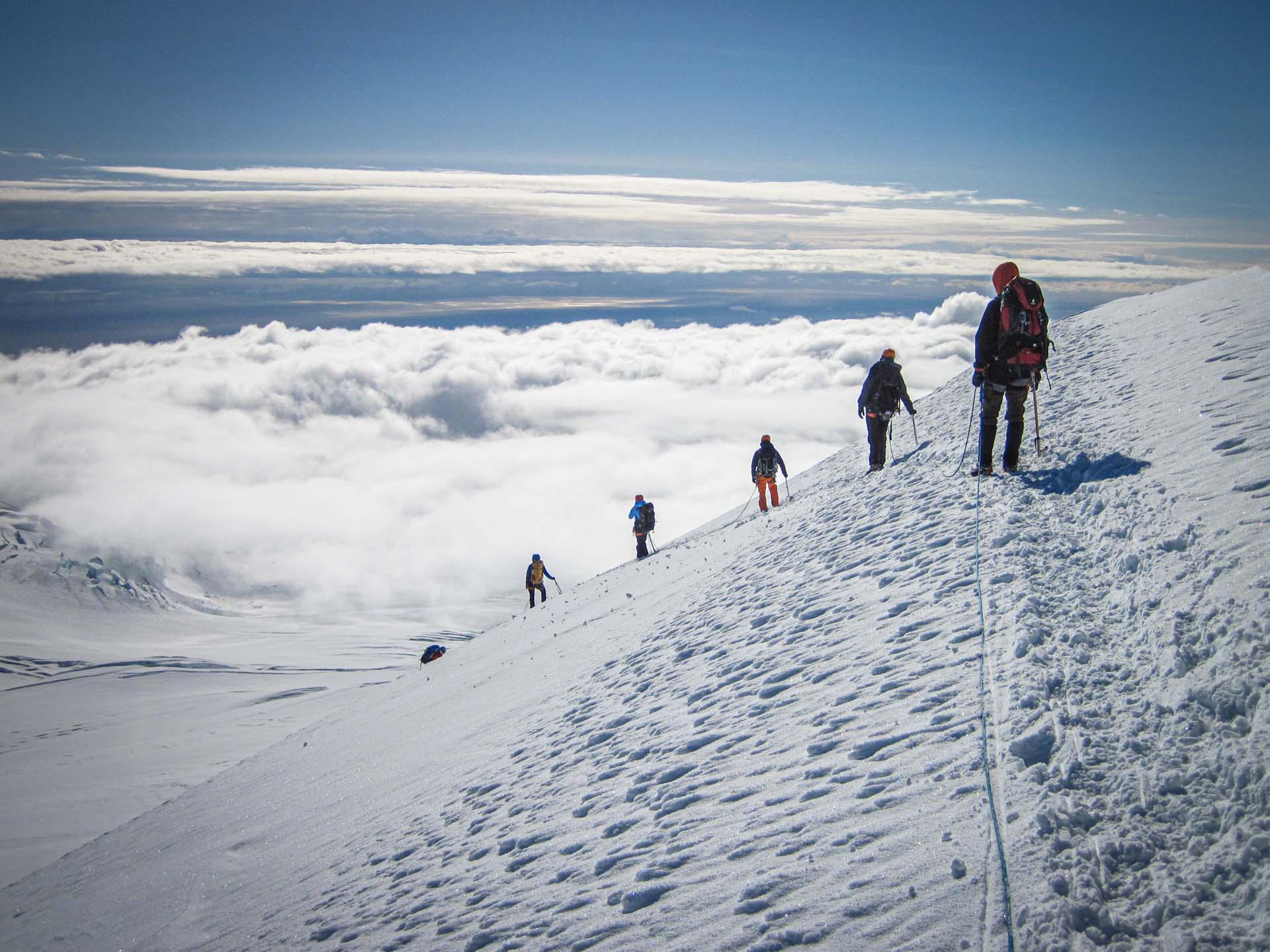 people doing down a snowy mountain above the clouds