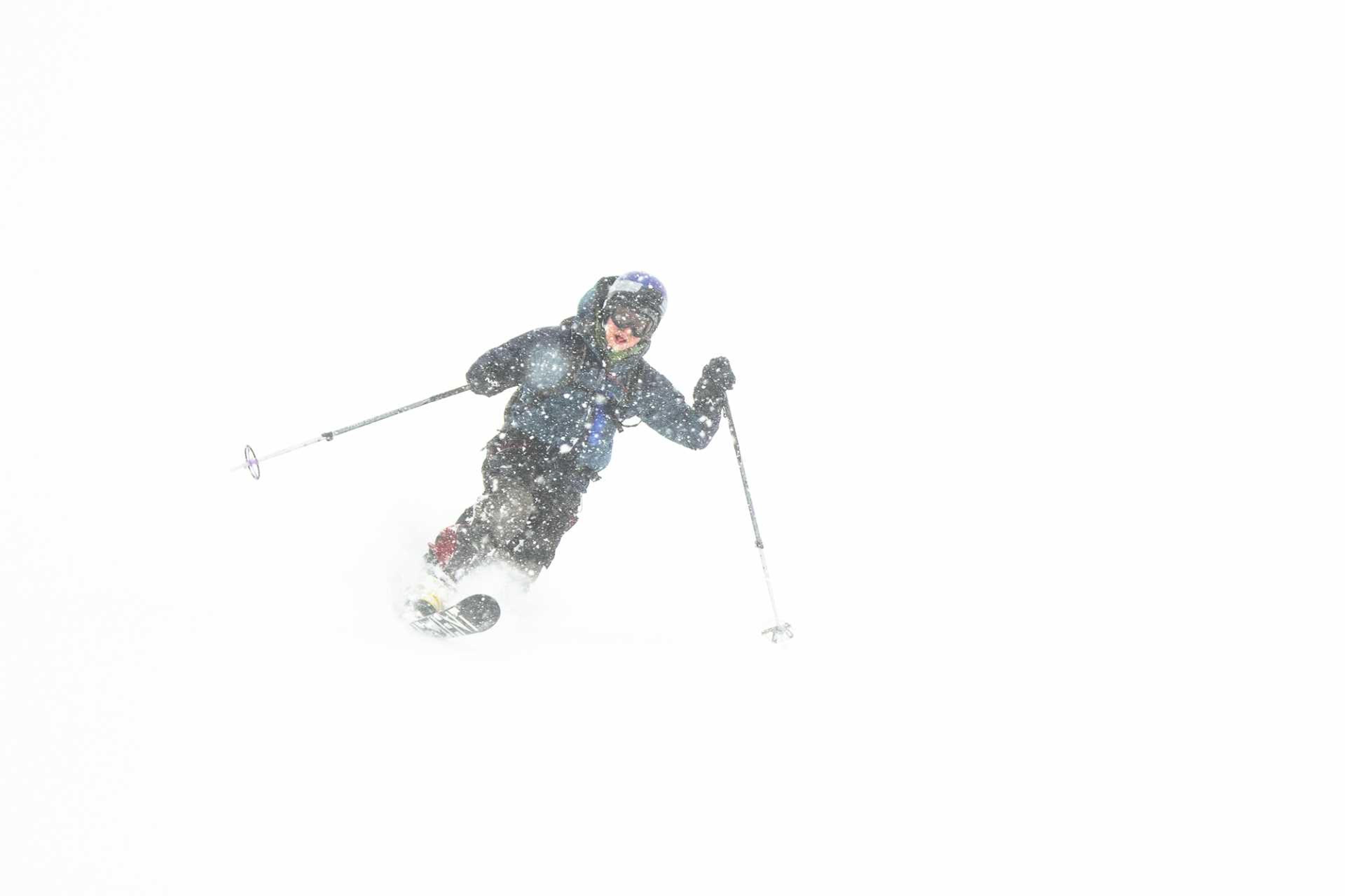 A skier carves through heavy snowfall, blending into the whiteout conditions of the icy landscape.