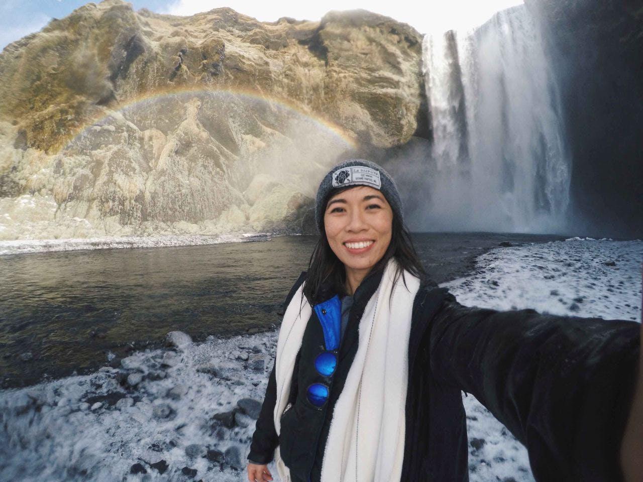 woman standing in front of a warerfall and a rainbow