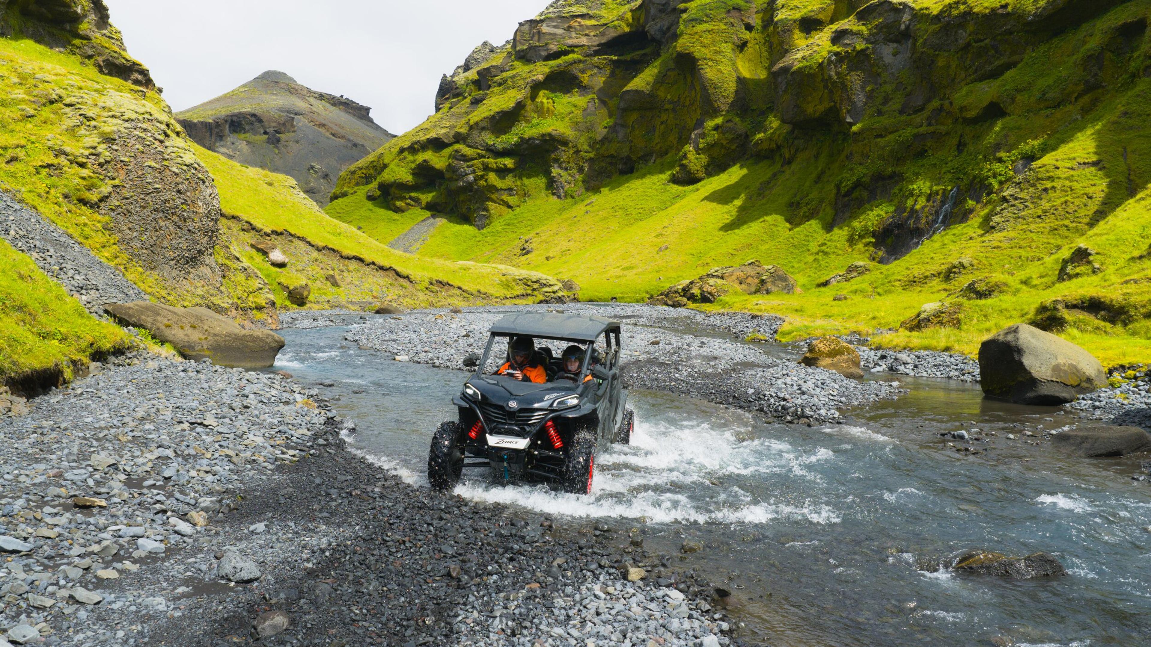 A family wearing safety gear on a buggy tour in South Iceland, with a 4-seater buggy in the foreground and a scenic coastline in the background.
