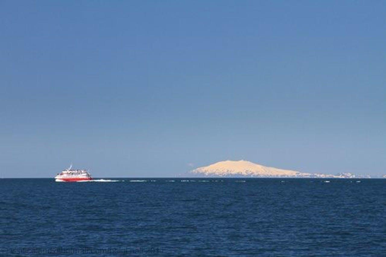 Snæfellsjökull glacier in the distance with a boat sailing in the sea in front of the glacier