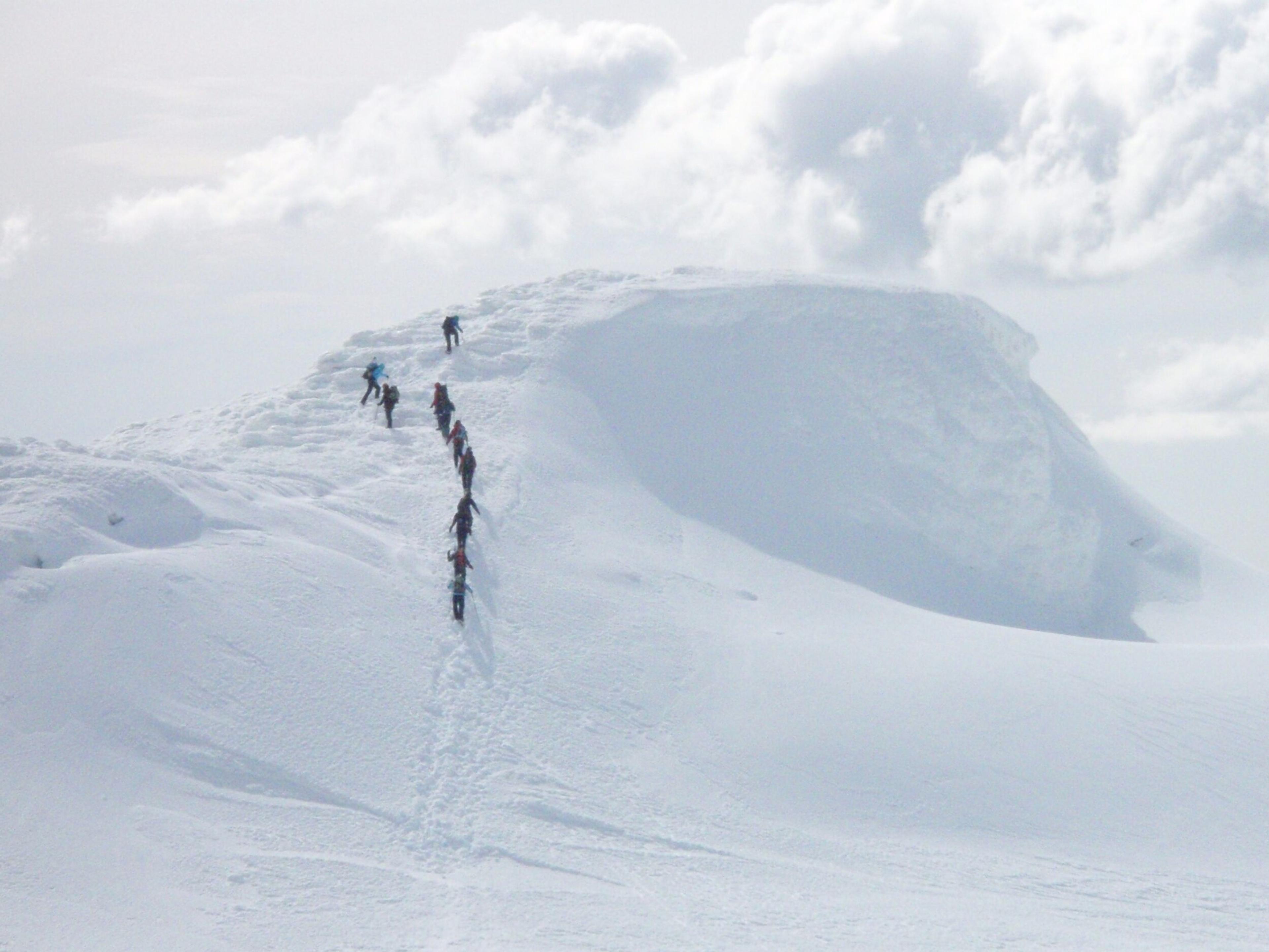 A group of six hikers, equipped with climbing gear, stands together on the snowy summit of Eyjafjallajökull glacier under a bright, clear sky.