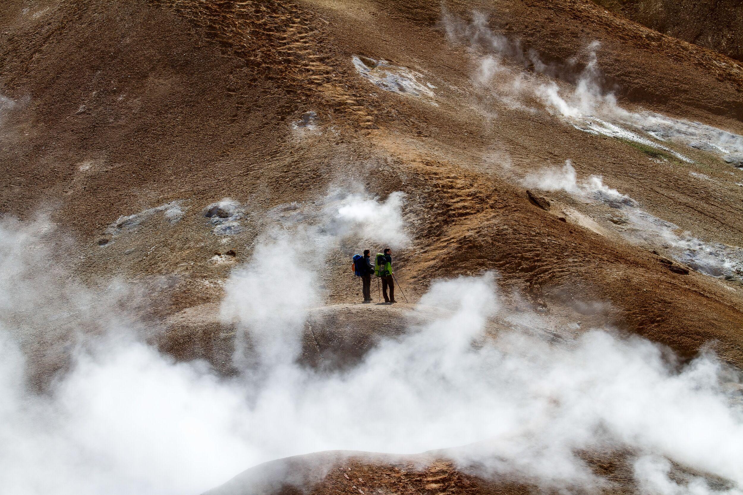 A lone hiker amidst steam vents and rugged volcanic landscape in Fjallabak Nature Reserve, Iceland.