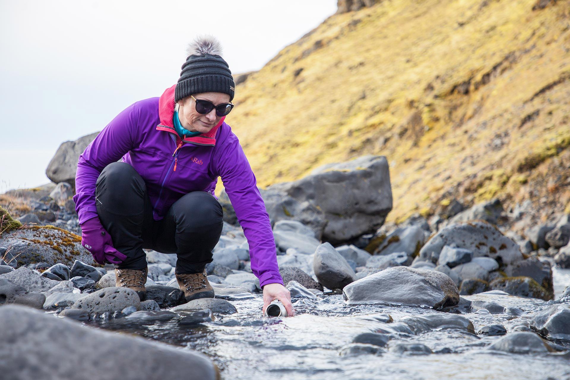 A woman getting some water into a bottle from a clean water stream