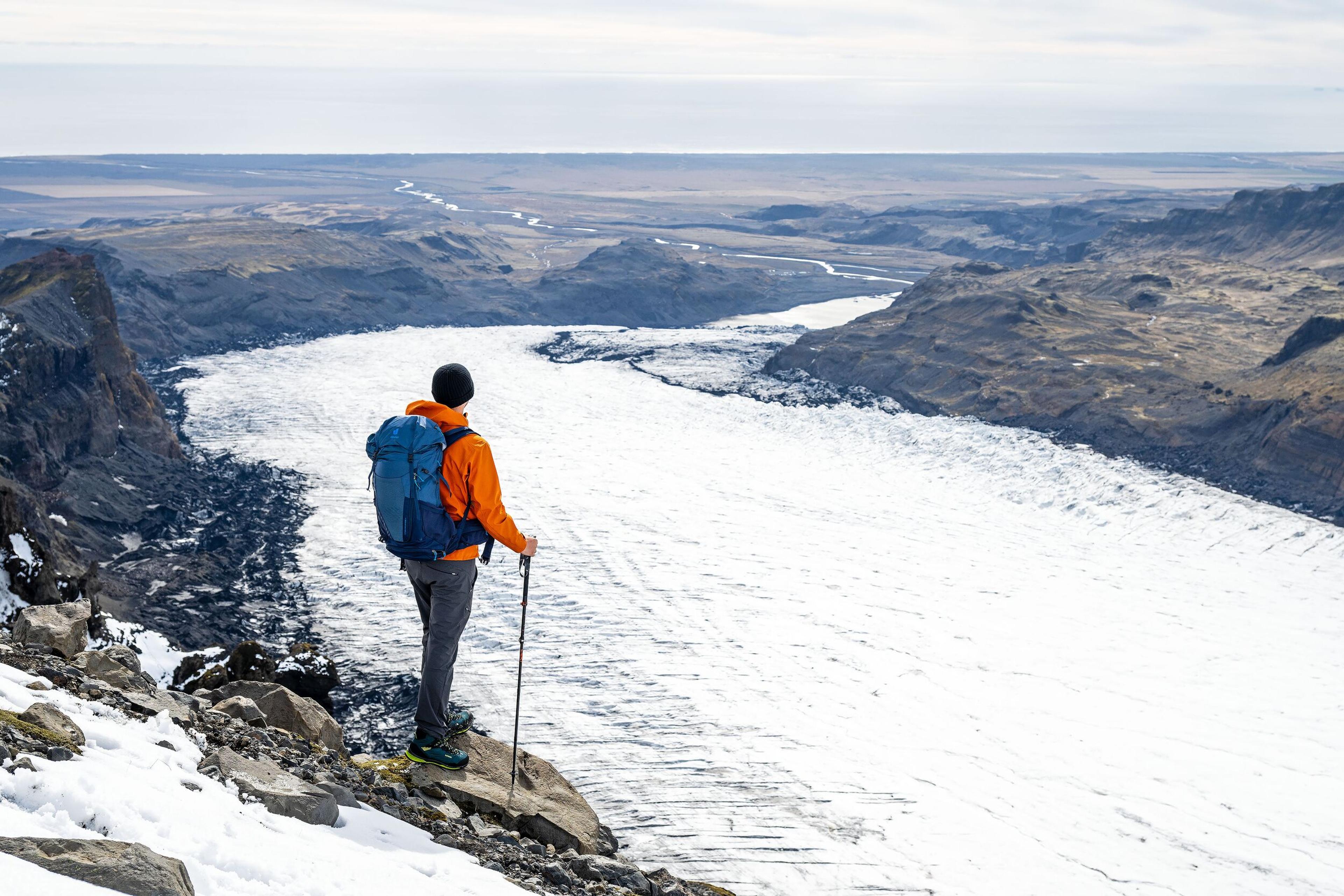 A hiker with a backpack looking over a massive glacier tongue below