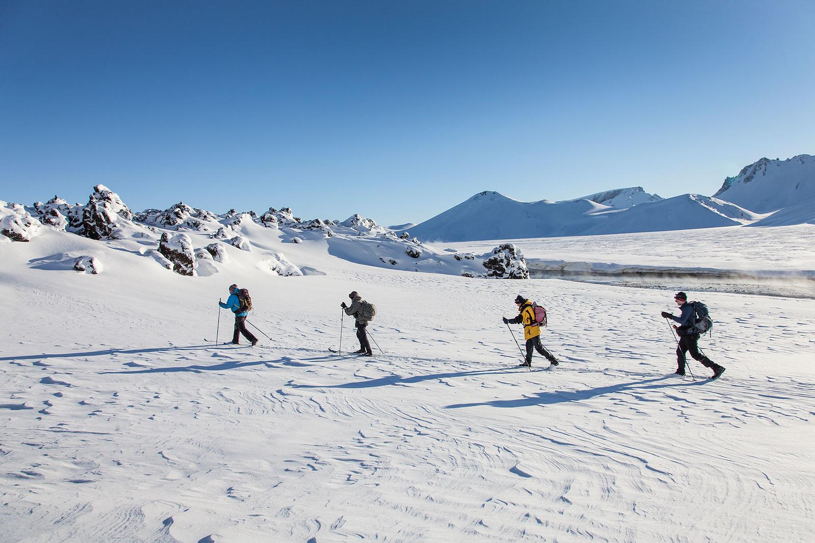 People hiking in snowy plains with snowy mountains and rocks in background