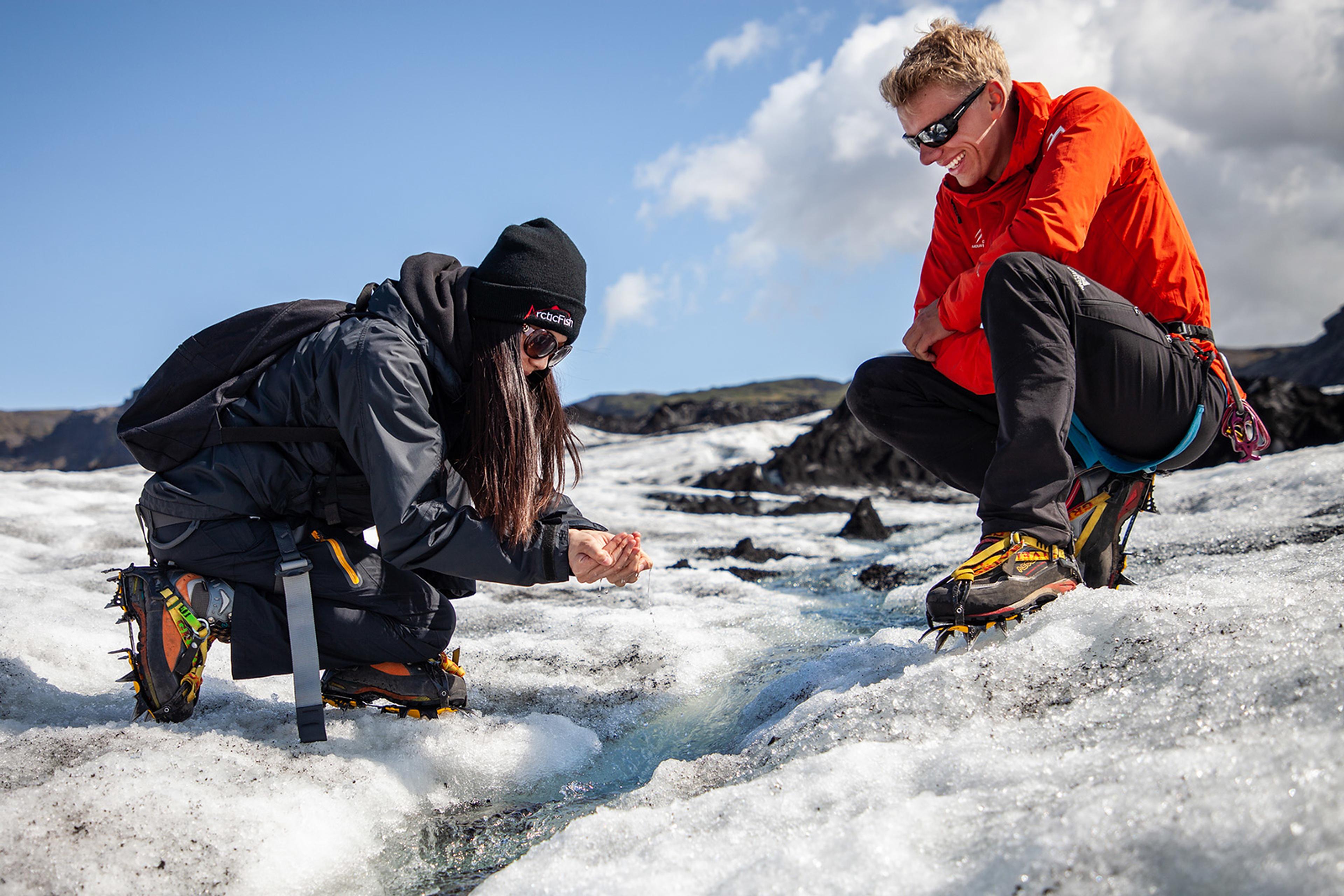 A woman and an Icelandic Mountain Guide enjoying real glacial water on Sólheimajökull