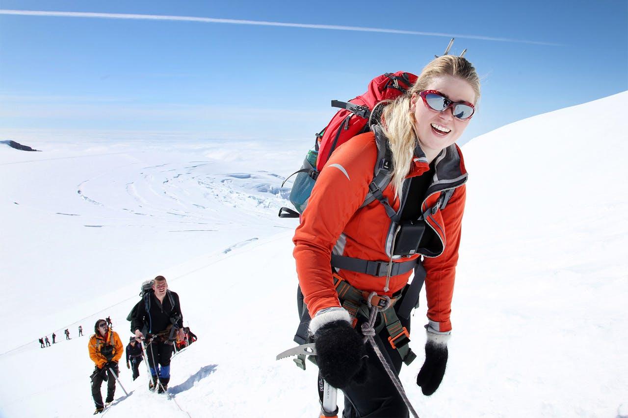 A woman in a red jacket smiling while hiking up to Iceland's highest peak