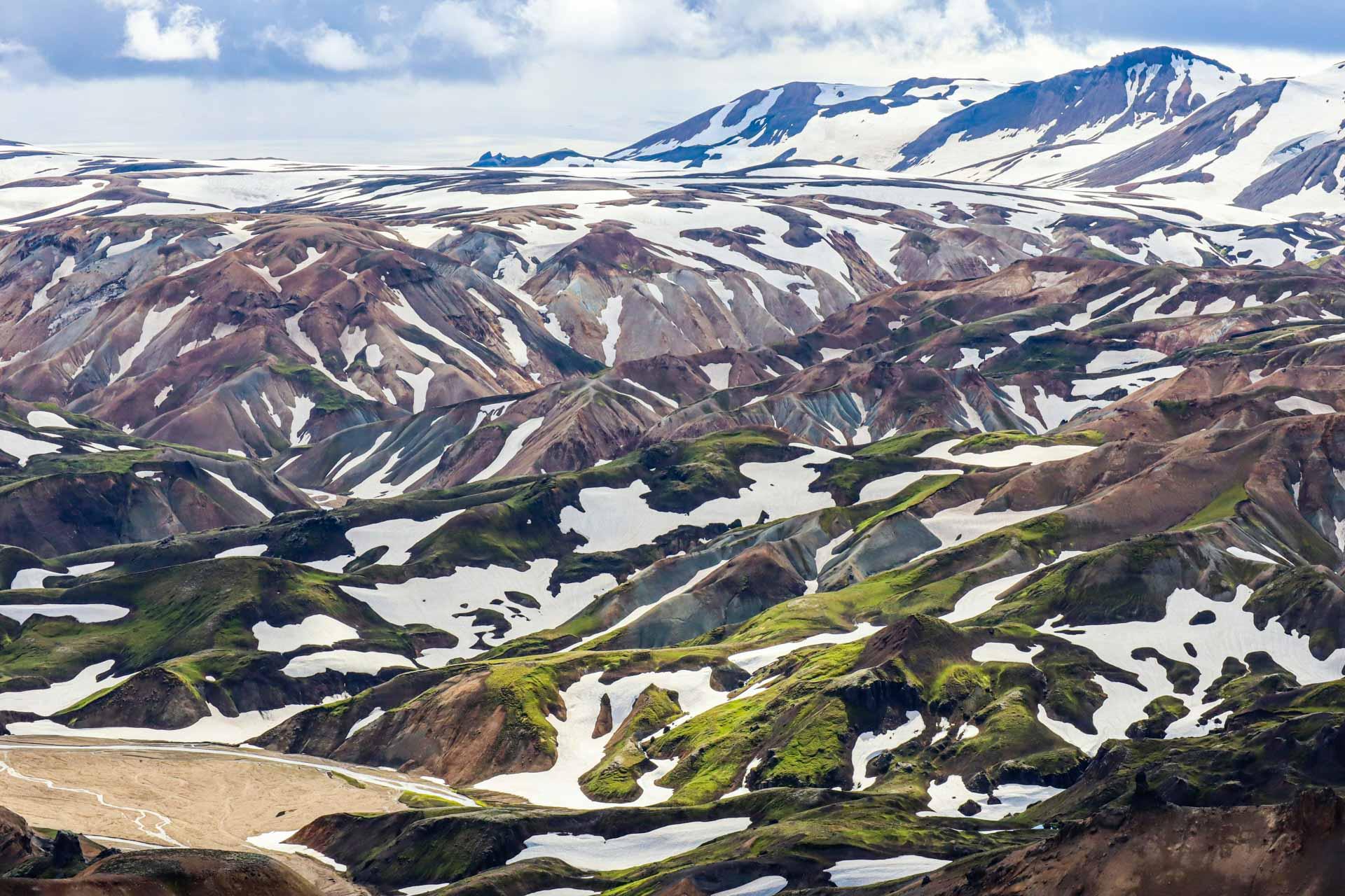 Colorful, snow-speckled mountains with lush green patches in Fjallabak Nature Reserve, Iceland.